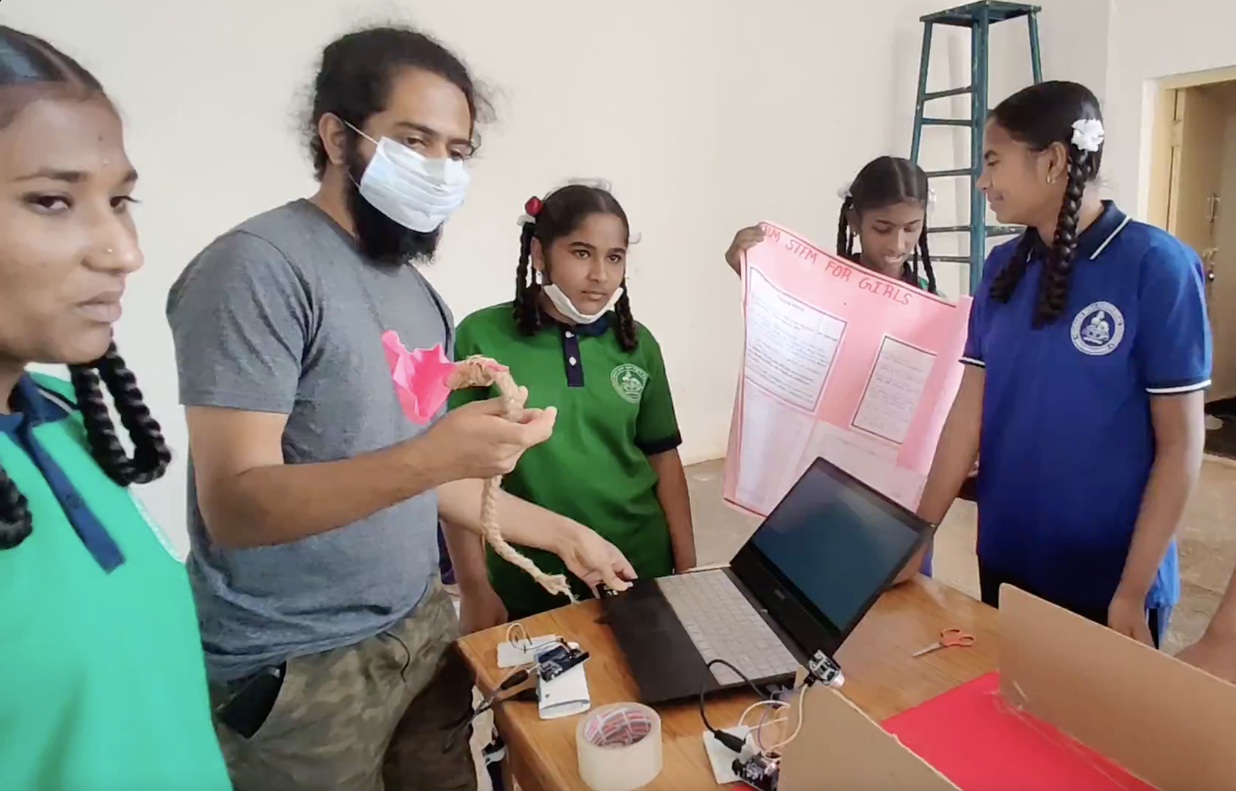 A member of our team standing with a group of students at a hackathon showcase event in a government school we work in, along with a laptop, a breadboard, and an arduino microcontroller-based device made by the students.