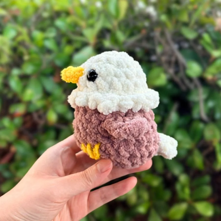 side view of a little crochet bald eagle held up by a hand - free amigurumi crochet eagle pattern