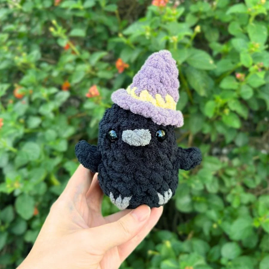 little amigurumi crochet no sew raven with a gray beak and feet and a tiny crochet purple witch hat - free crochet pattern