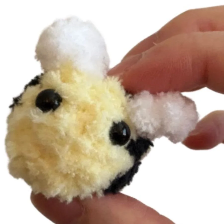a tiny crochet yellow bee with white wings held between fingers - free crochet bee pattern