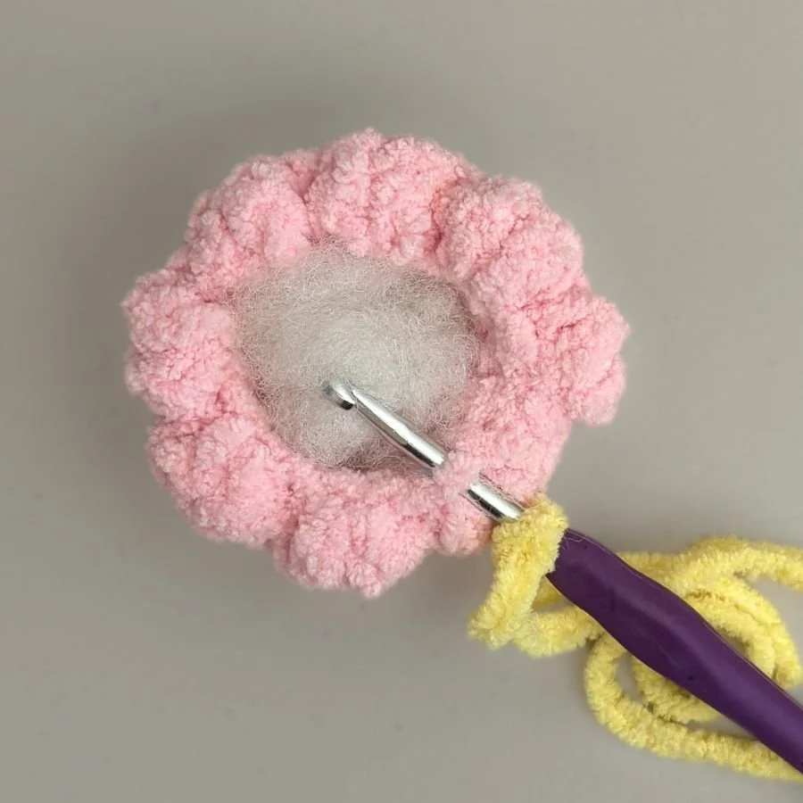 crochet hook with a yellow slip knot on it it, inserted into the back loop inside the rim of the pink crochet eggshell