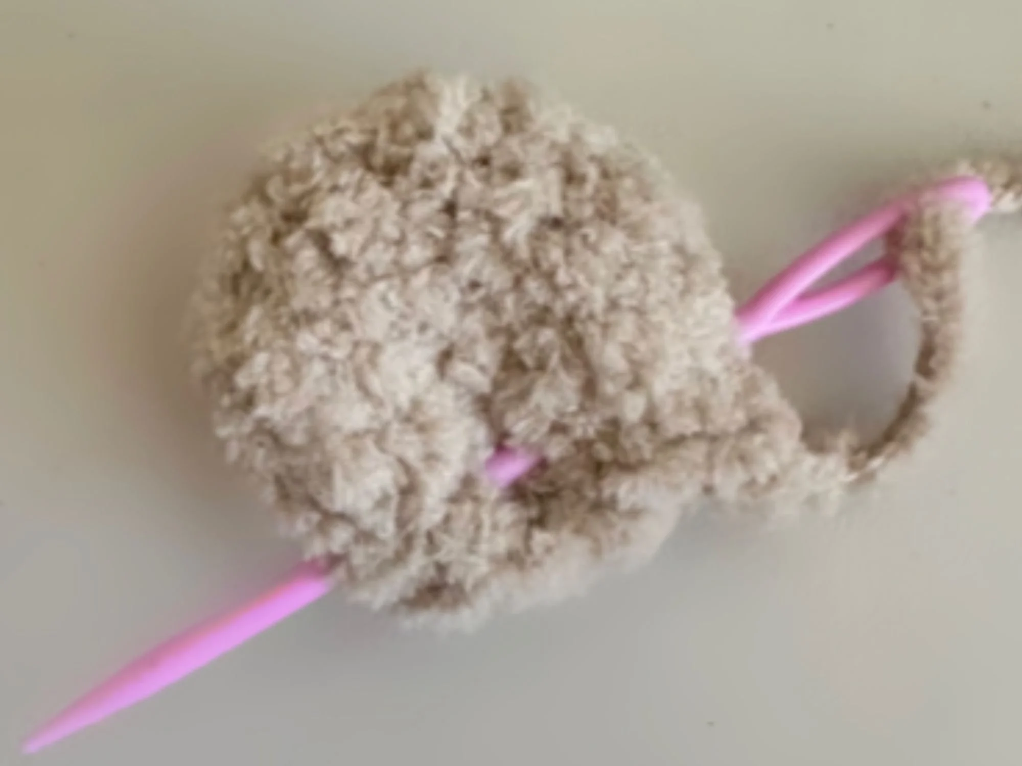 reference photo on how to sew across ear of the bear with a pink needle inserted along the bottom of the ear.