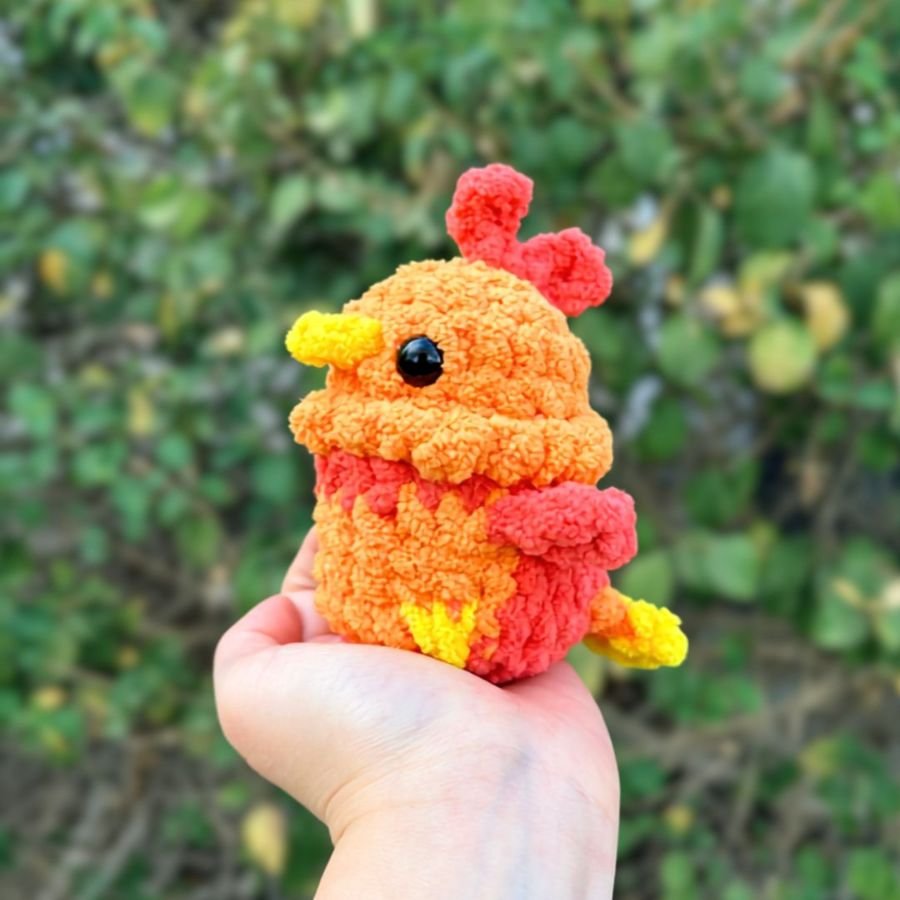 small amigurumi phoenix in red, orange, and yellow held in the palm of a hand - free crochet phoenix pattern
