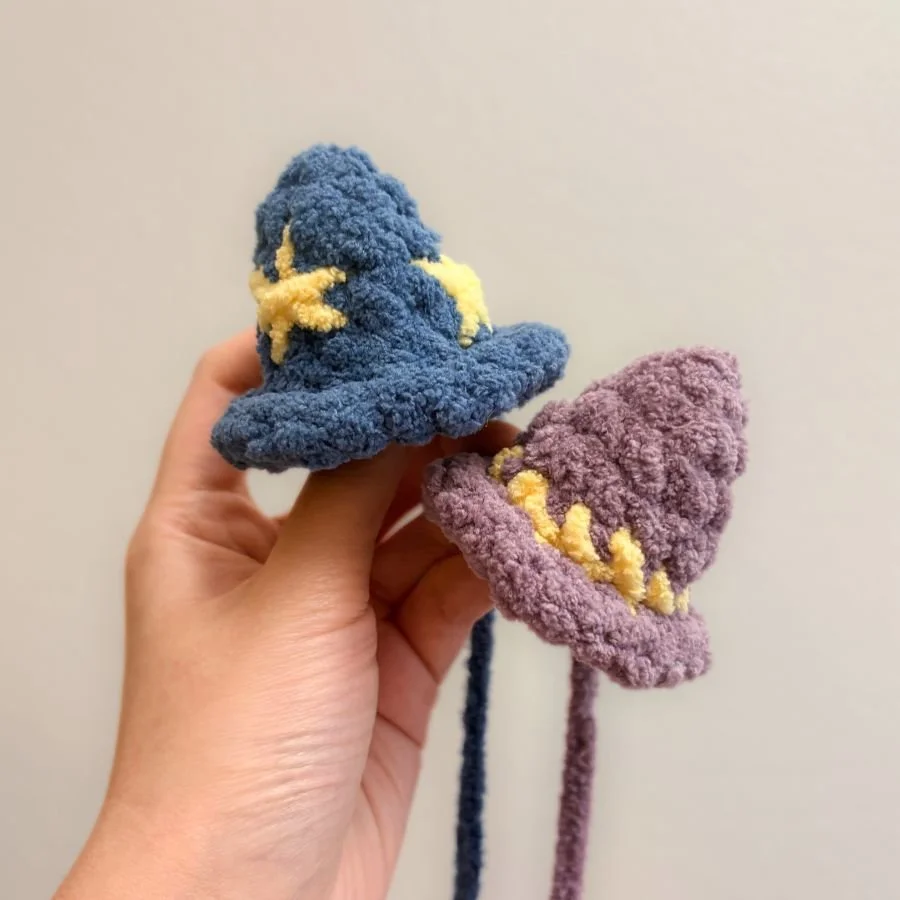 little crochet blue wizard hat with yellow stars and a little crochet purple witch hat with a yellow stripe held with a hand and made with blanket yarn - free crochet pattern - mini crochet hats