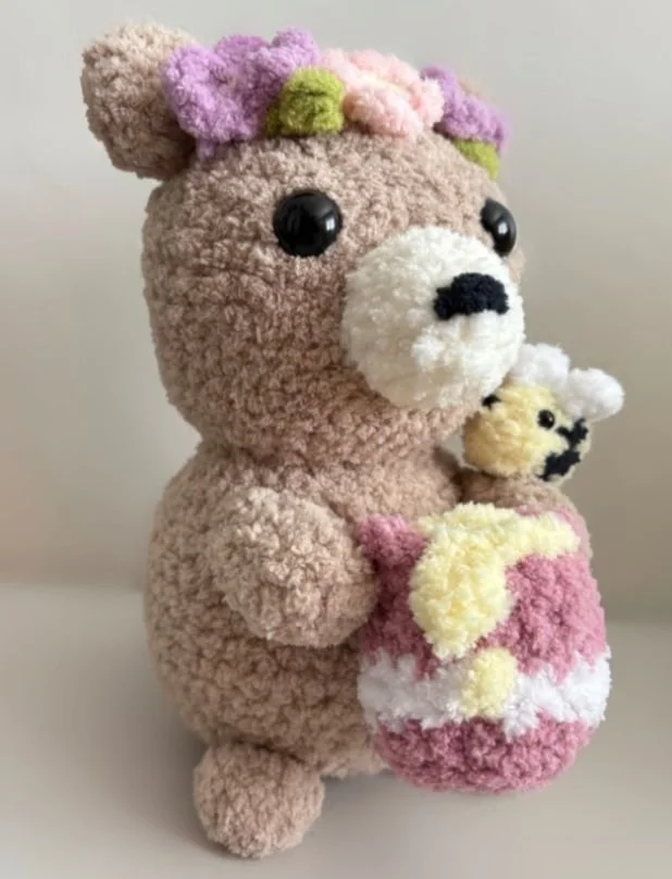 crochet honey bear holding a honey pot with a dripping honey and a drop of honey on the stripe of the pot - free honey bear amigurumi pattern