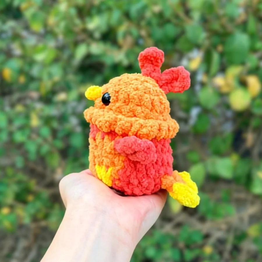 small crochet phoenix made with red, orange, yellow yarn held by a hand - free no-sew amigurumi phoenix pattern