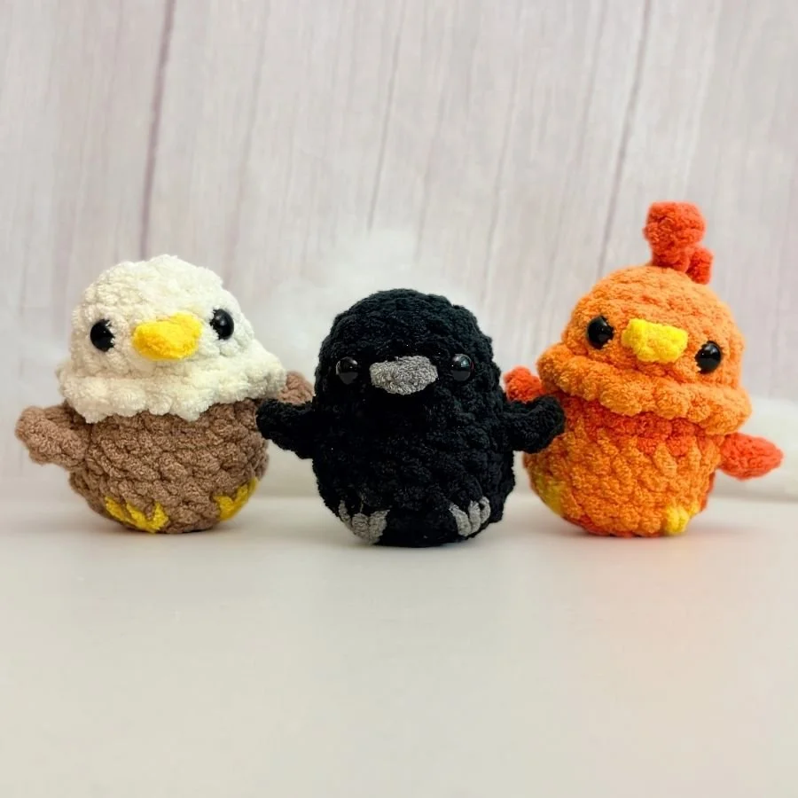 three little no-sew crochet birds including a little eagle, little raven, little phoenix, sitting on a white table - free amigurumi pattern