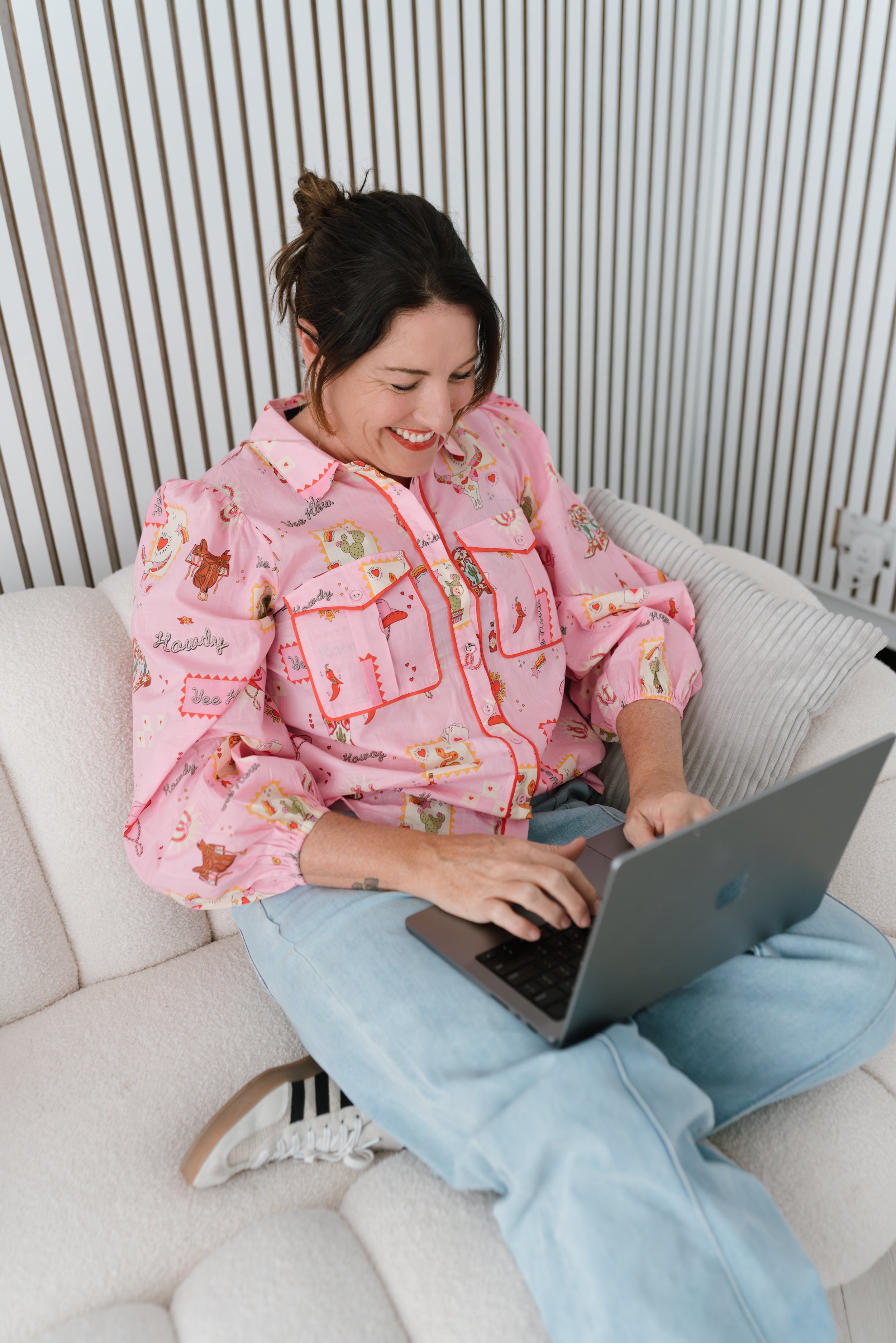 Melbourne legals only celebrant Nat Sproal in jeans and a pink Western style blouse working on a laptop.