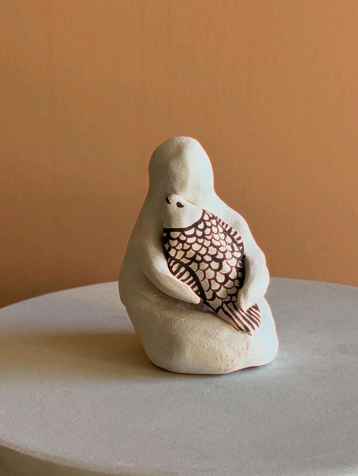 ⁨	پیکره&zwnj;ای خاموش،
با ماهی&zwnj;ای در آغوش؛
انگار جانِ ظریفی را میان اندوه و امید در خود نگه داشته است.

ماهی برای من نشانه&zwnj;ی زندگی&zwnj;ست؛
نشانه&zwnj;ی حرکت، ادامه&zwnj; داشتن،
و نوری که حتی در تاریکی هم خاموش نمی&zwnj;شود.
این اثر را به ی