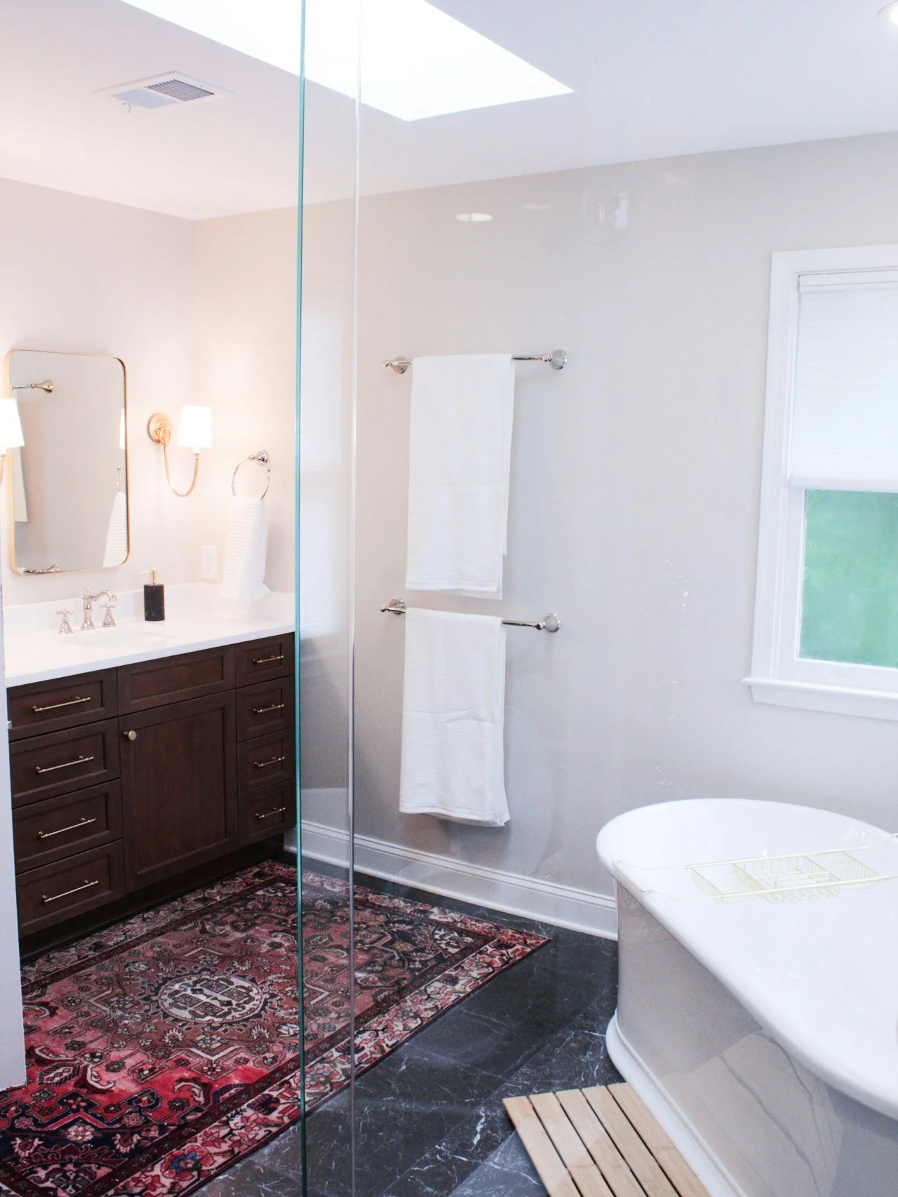 Rich wood cabinetry, soft lighting, and a vintage rug add warmth and personality to this Matthews bathroom space ✨🤎