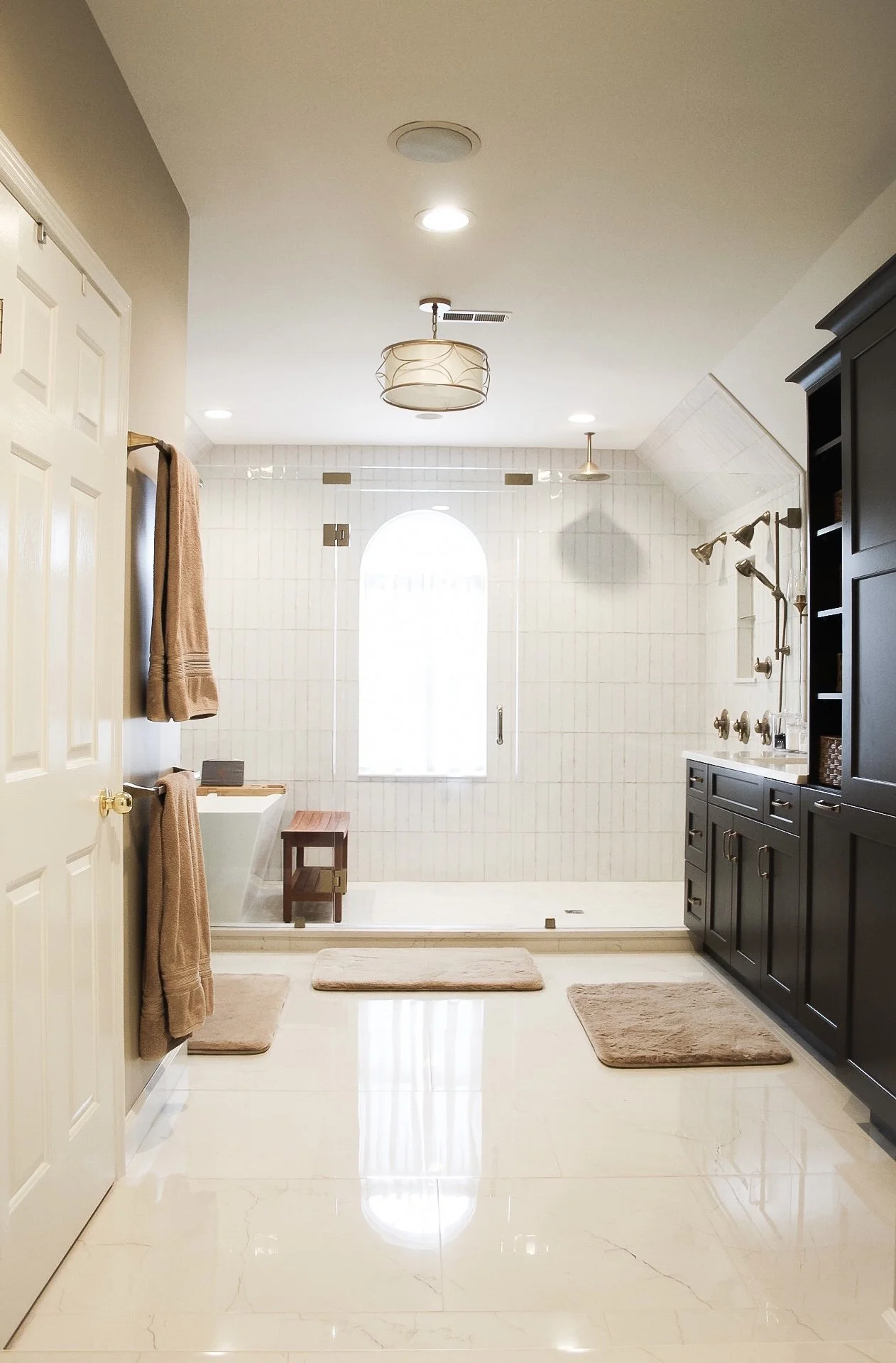 Bright modern bathroom with a walk-in shower, black cabinetry, beige towels, and a large arched window.