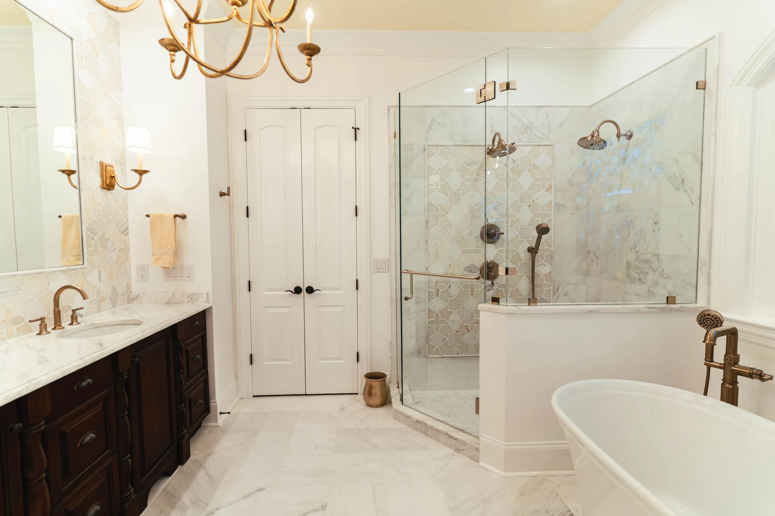 Matthews Bathroom Showcasing Rich dark wood cabinetry, a beautiful white tub, and a statement gold chandelier.