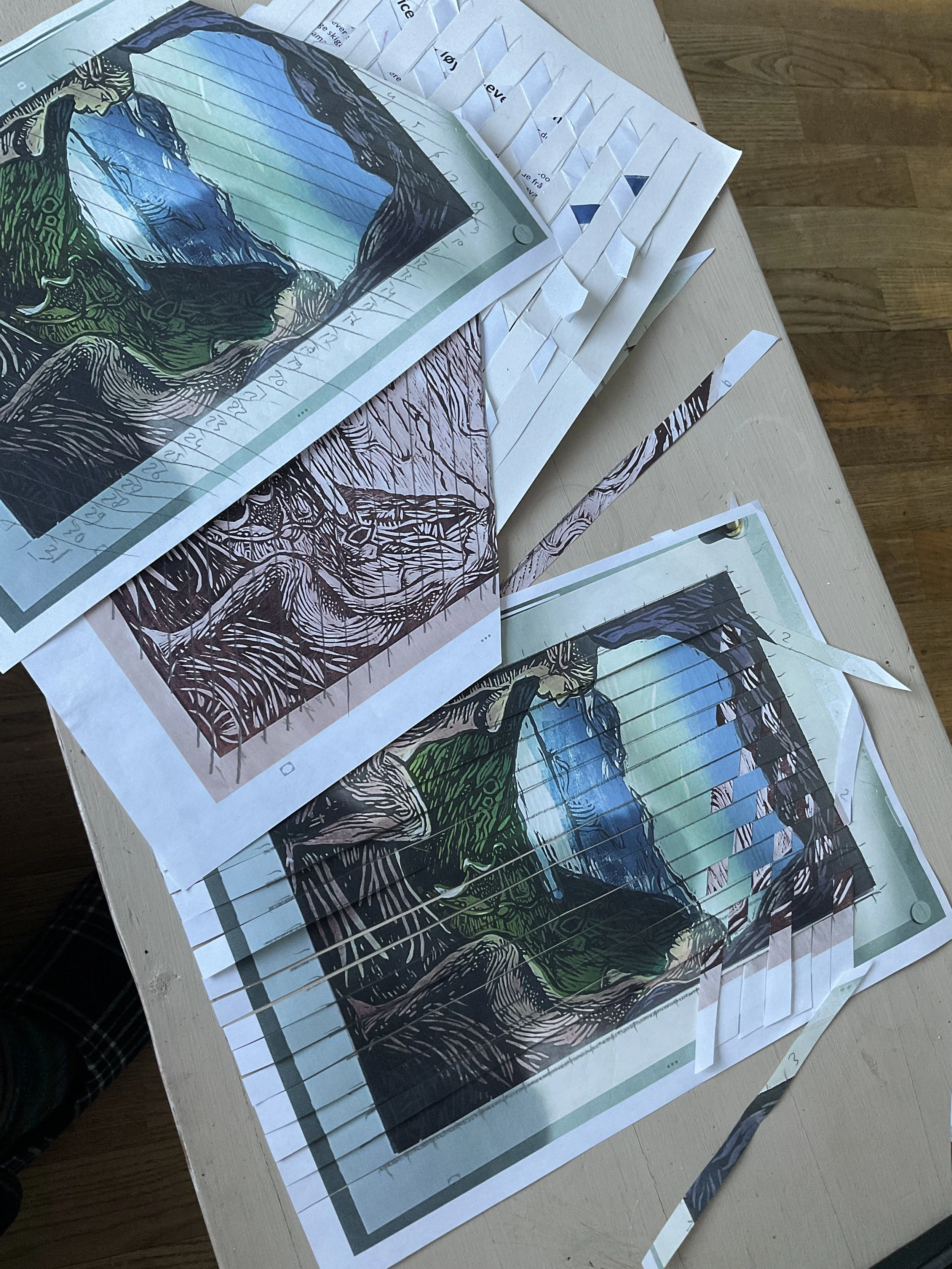 Colorful woodcut prints of a mountain scene laid out on a table, with some paper cutouts and hidden lined paper beneath.