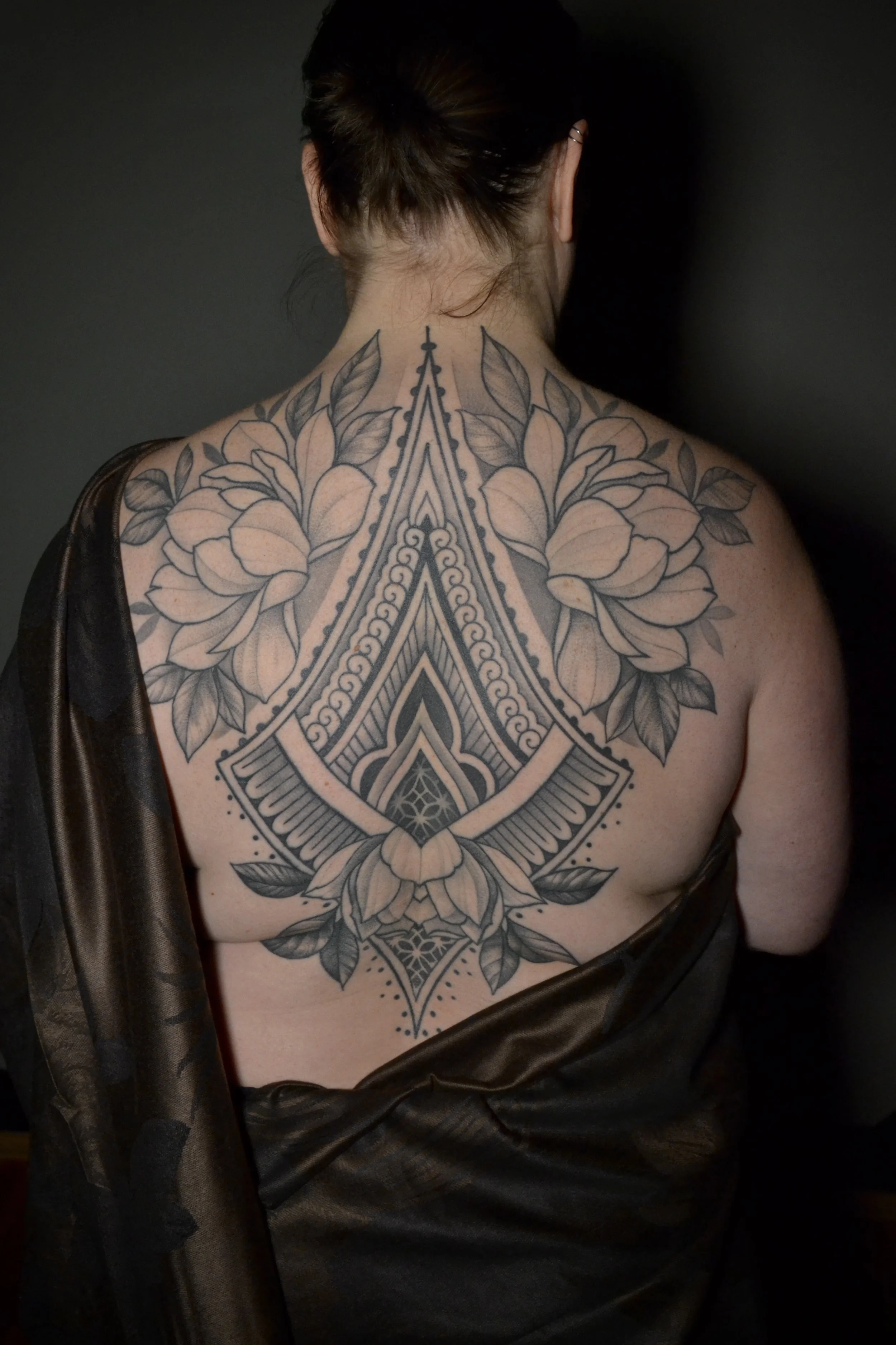 Floral ornamental backpiece tattoo with bold lines and smooth shading, designed and tattooed by Maya Wild at Sub Rosa Tattoo Studio in Grants Pass, Oregon. This intricate piece highlights symmetry and botanical details. Ideal for clients looking for 