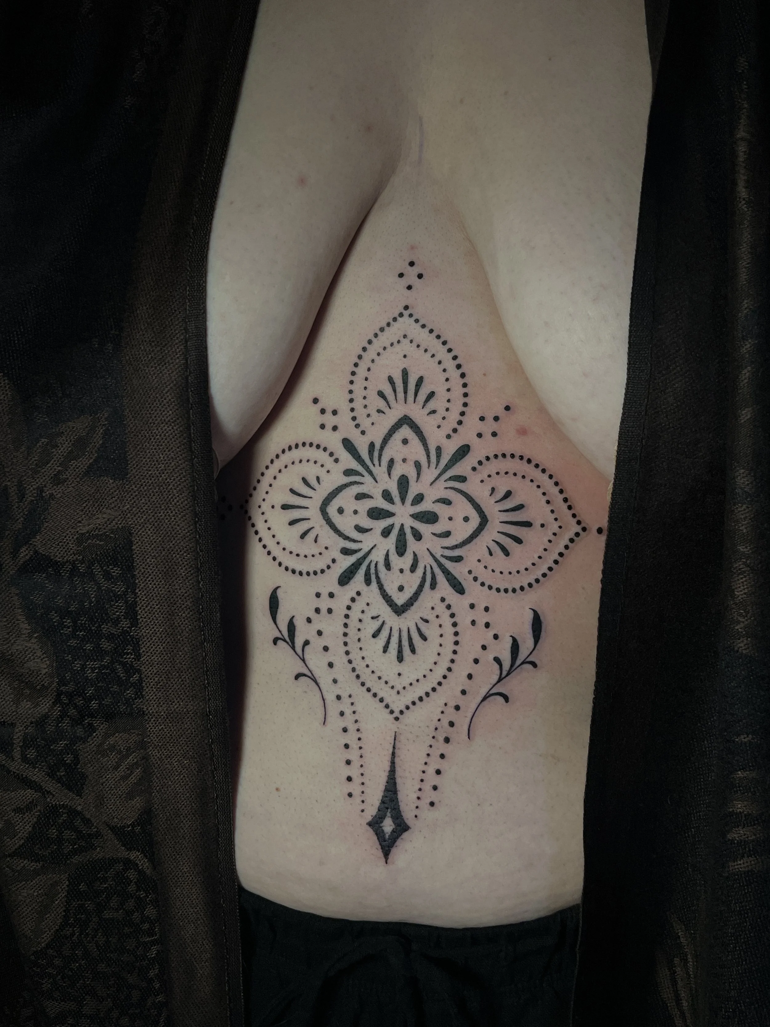 Ornamental dotwork sternum tattoo with high contrast details, designed and tattooed by Maya Wild at Sub Rosa Tattoo Studio in Grants Pass, Oregon. This intricate piece highlights precision and symmetry to flatter the chest and stomach. Ideal for clie