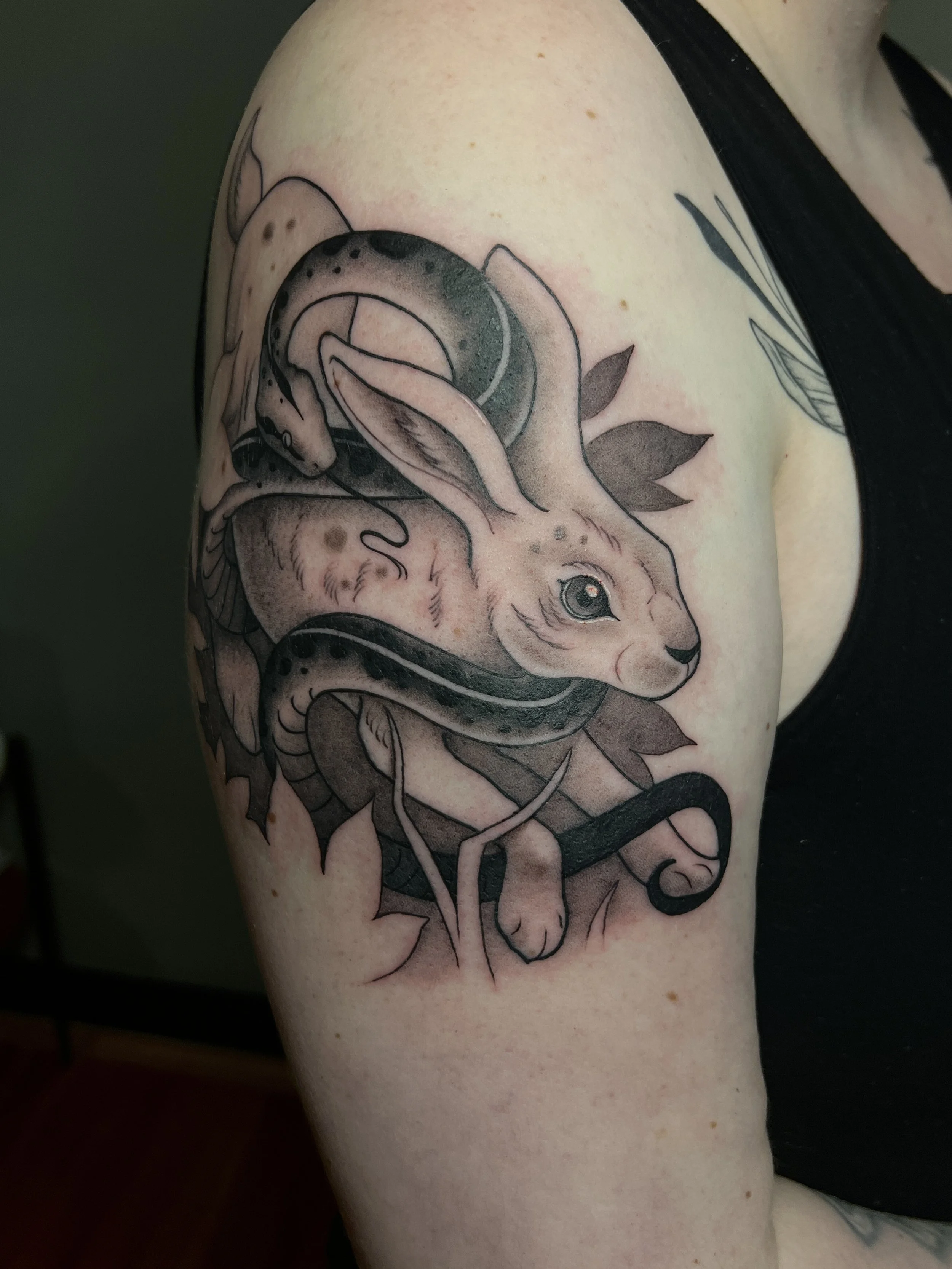 Illustrative snake and rabbit arm tattoo with botanical and negative space elements, designed and tattooed by Maya Wild at Sub Rosa Tattoo Studio in Grants Pass, Oregon. This unique piece highlights bold contrast and soft  details. Ideal for clients 