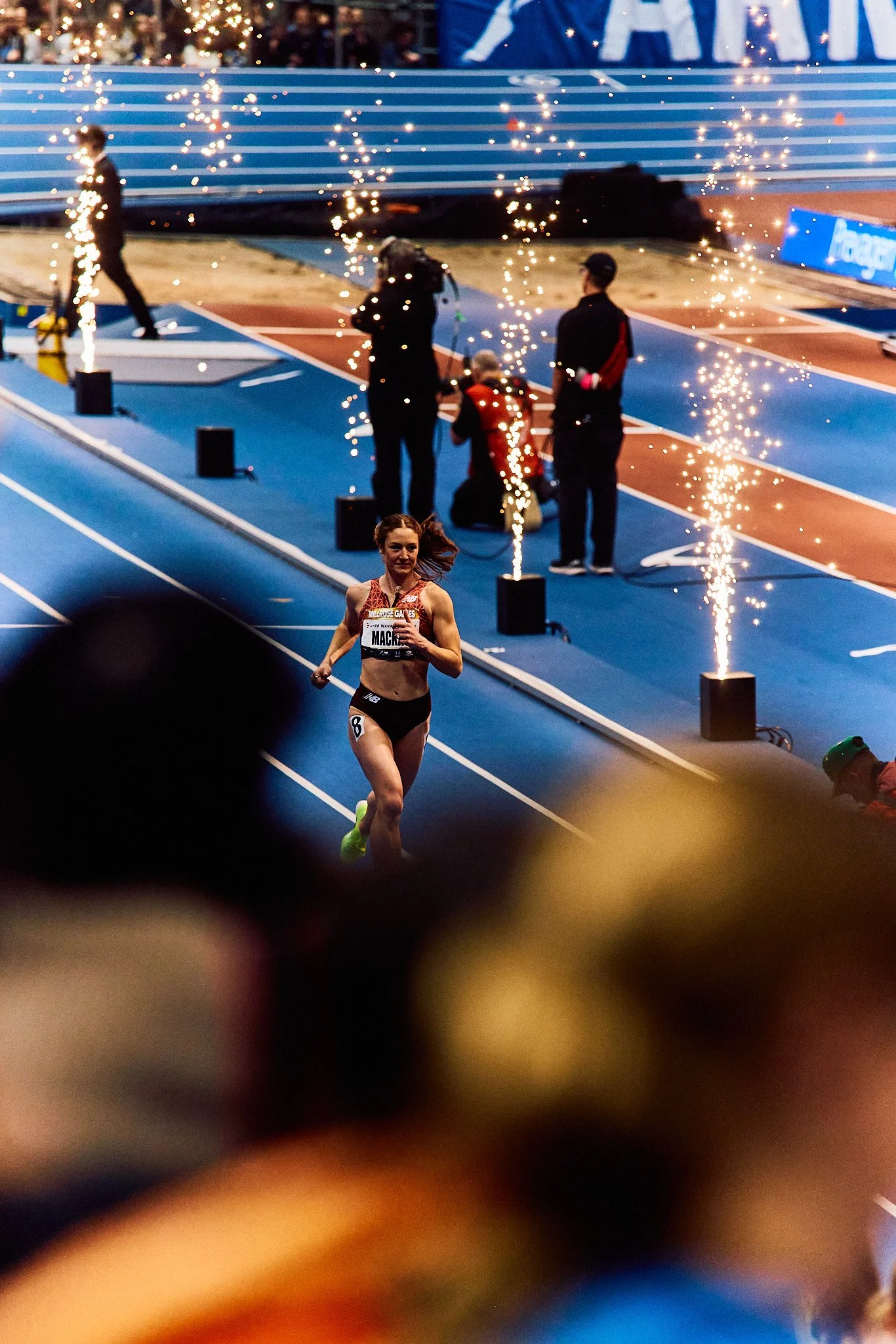 Female athlete running on a track during a race with fireworks in the background.