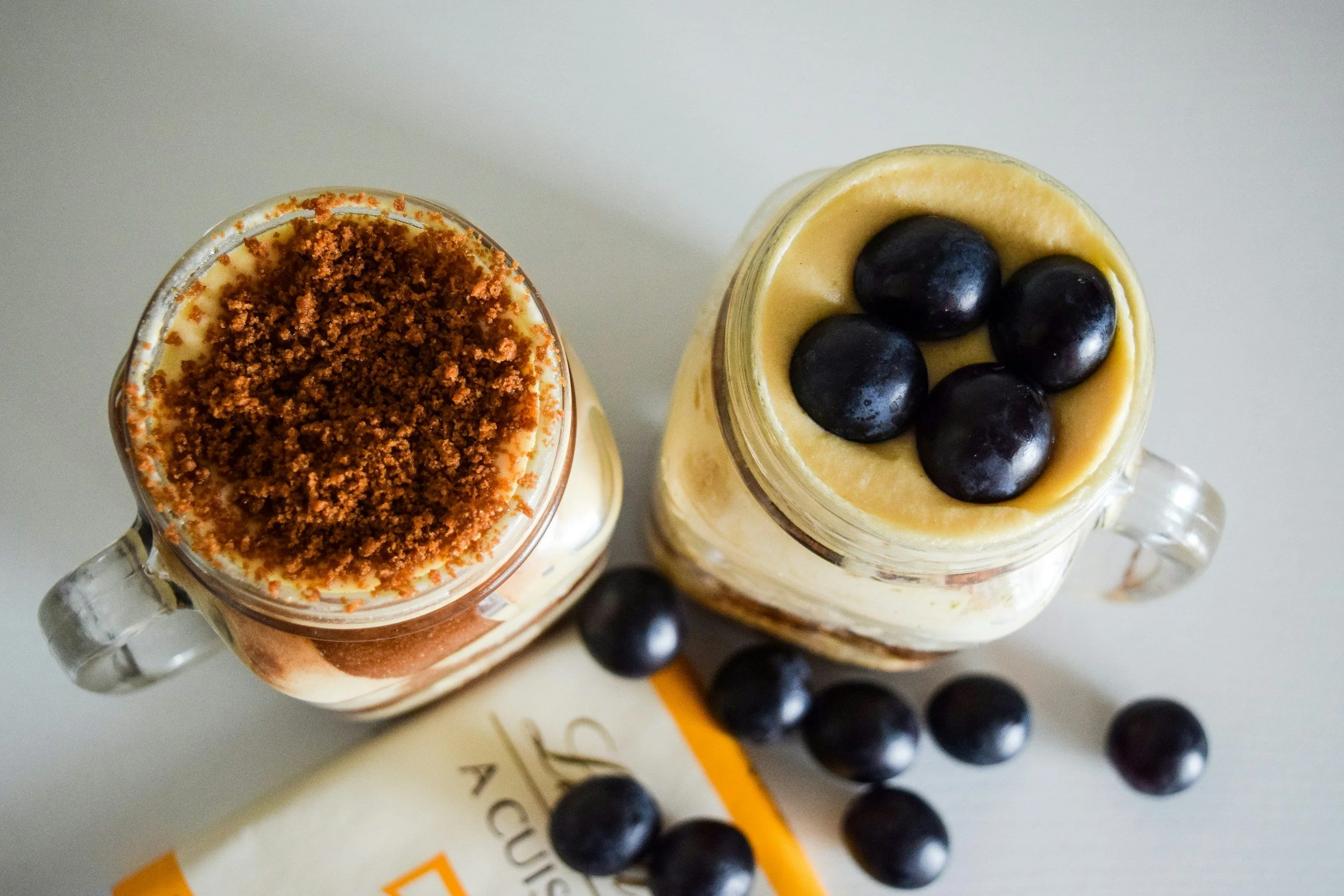 Two mason jar glasses with vanilla pudding topped with crumbled cookies and fresh blueberries on the side.