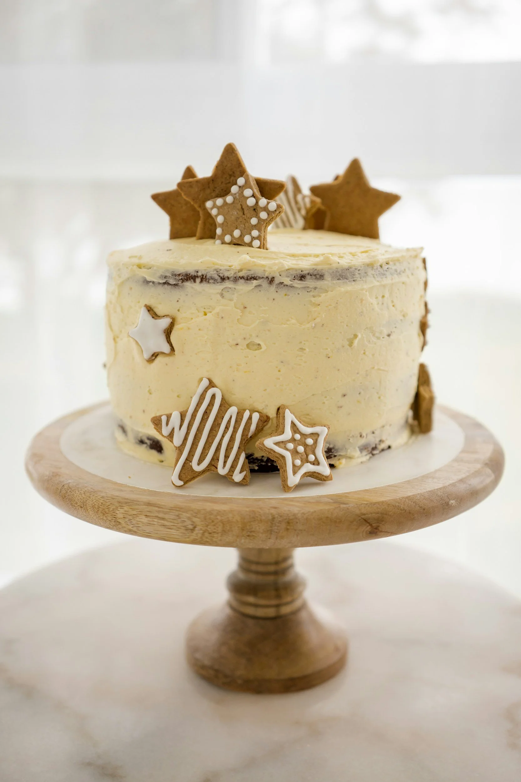 A birthday cake decorated with white icing, star-shaped cookies, some with white icing and sprinkles, on a wooden cake stand.