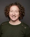 A smiling person with chin-lengthen, red, curly hair.