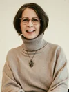 A smiling woman with short hair in a beige turtleneck sweater