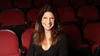 A woman with long hair in a dark shirt in a theater seat