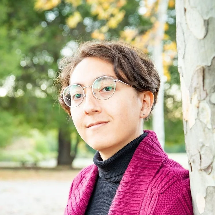 A person with short wavy hair and glasses looks up over a script