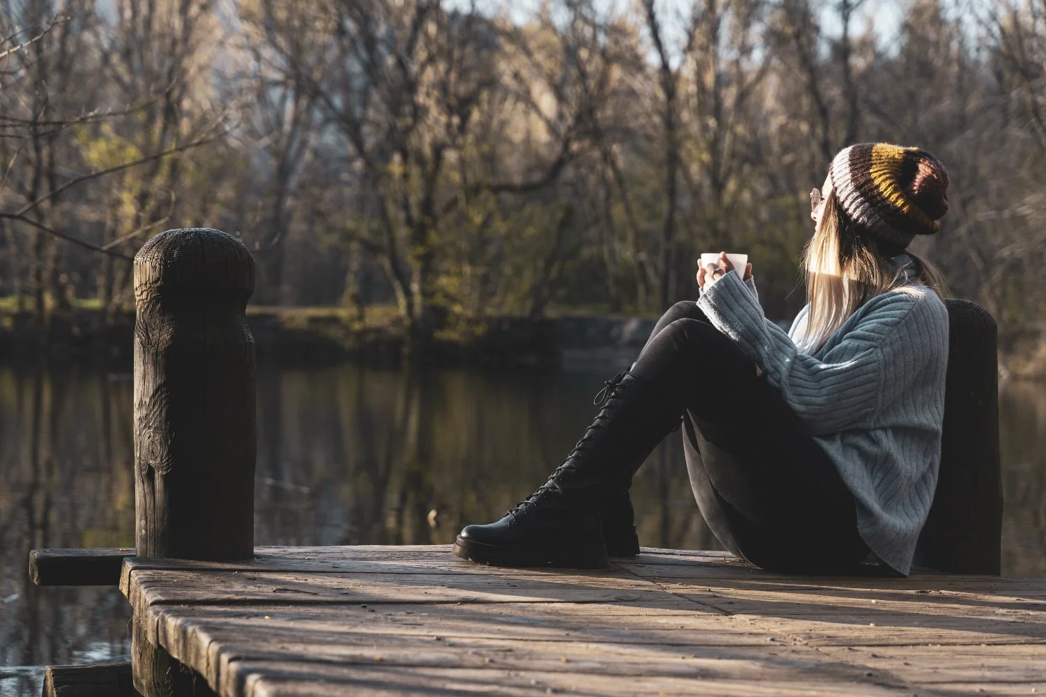 A person sitting quietly by the water, reflecting and resting, representing Manifestor energy, self-trust, and integration in Human Design.