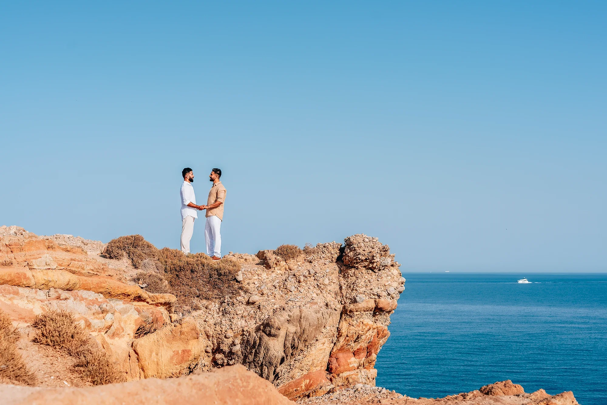Couple holding hands on a dramatic coastal cliff in Naxos with the Aegean Sea behind them