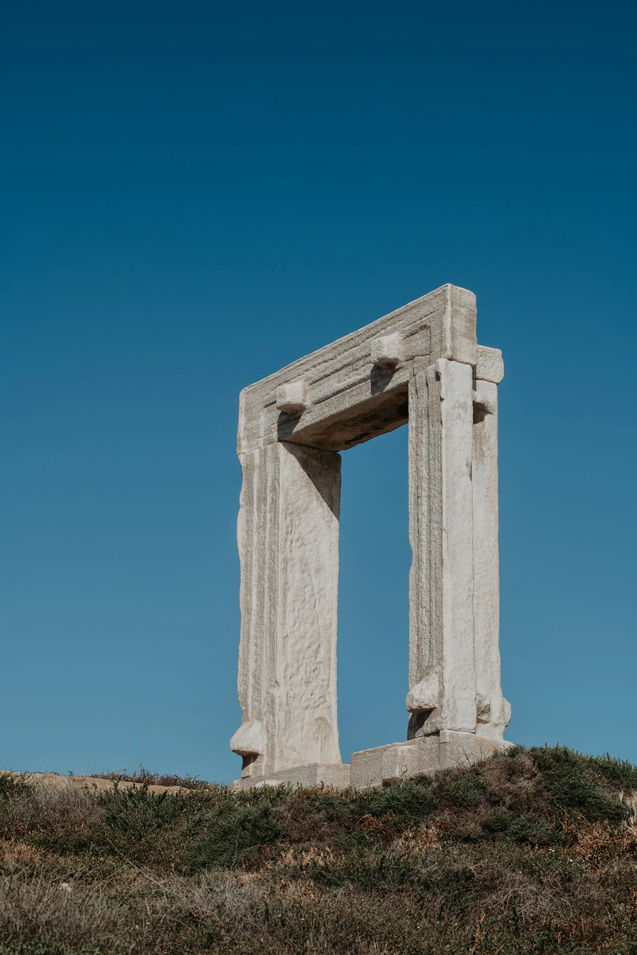 Landscape photography of the Portara Temple of Apollo in Naxos Greece standing on the hill with clear blue sky background