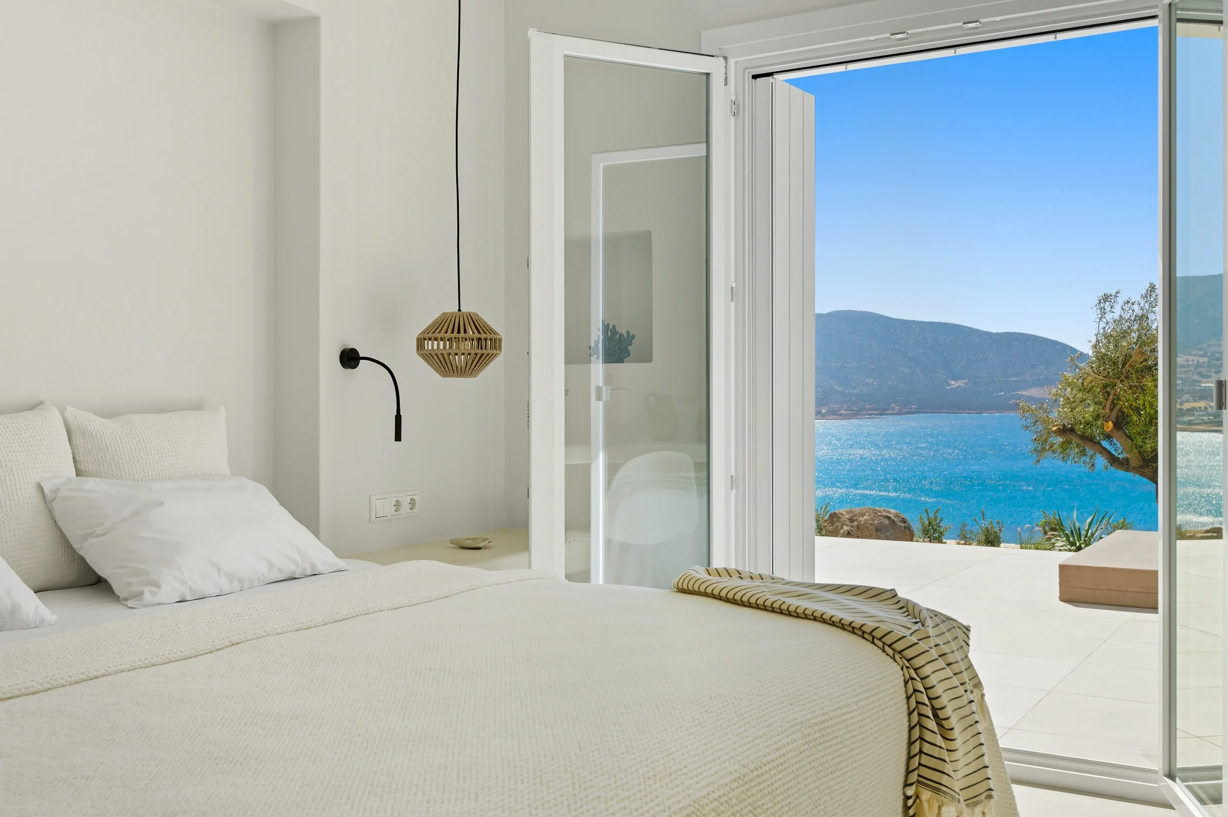 Luxury villa white bedroom with rattan pendant lamp and panoramic Aegean sea view — real estate photographer Naxos Greece