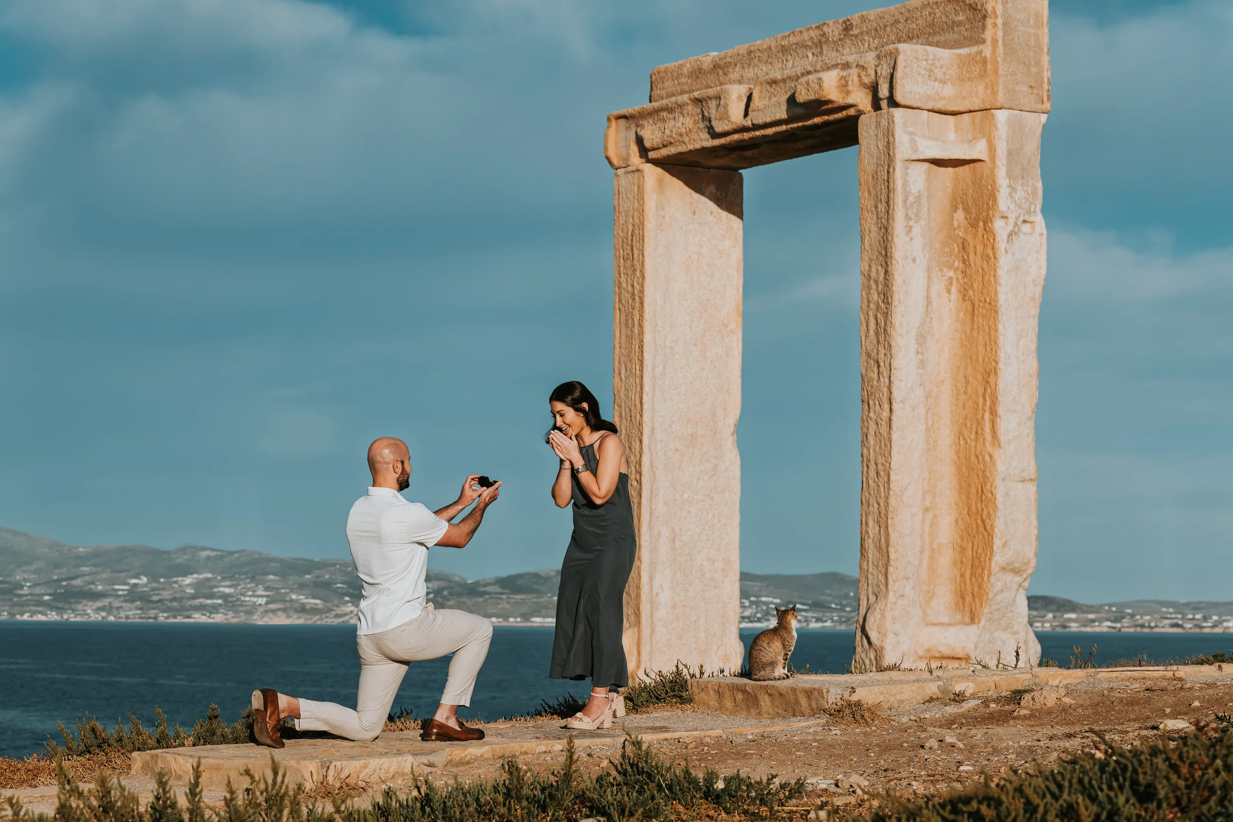 Romantic surprise wedding proposal at the Portara in Naxos, Greece, photographed by Naxos Photographer, Spyros Plakidas, with the Aegean Sea in the background.