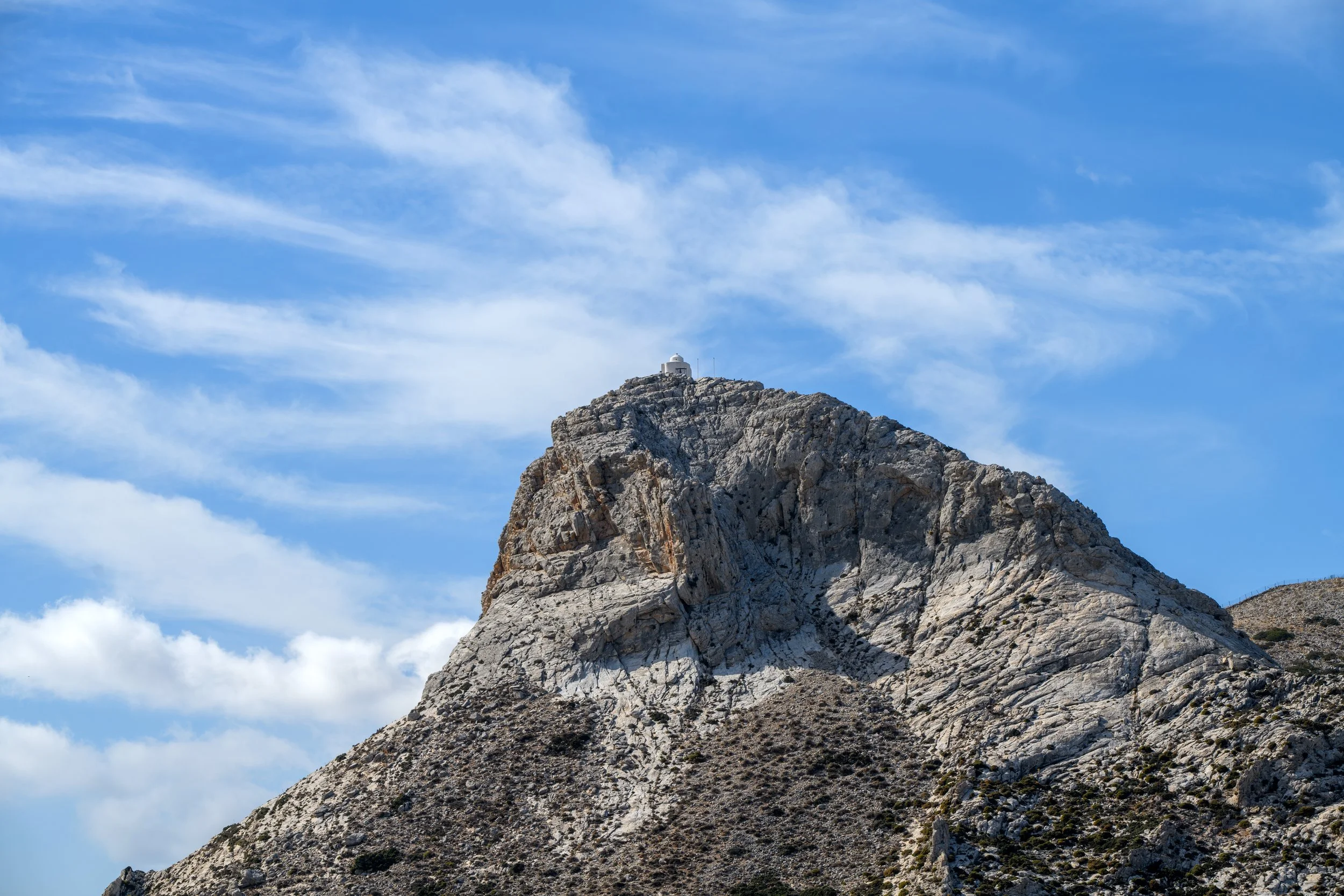 Landscape photography of the hilltop chapel above Filoti Village in Naxos Greece with rocky mountain peak and blue sky