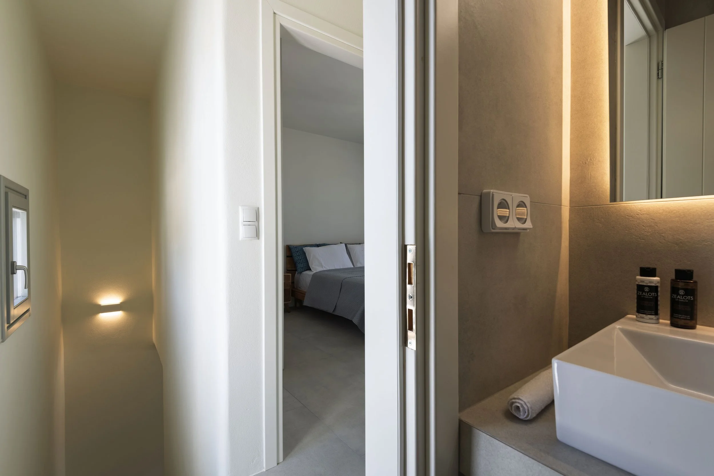 Modern hallway with stairwell lighting leading to a cozy bedroom and a bathroom with ambient lighting in Kastraki, Naxos – professional interior and real estate photography.