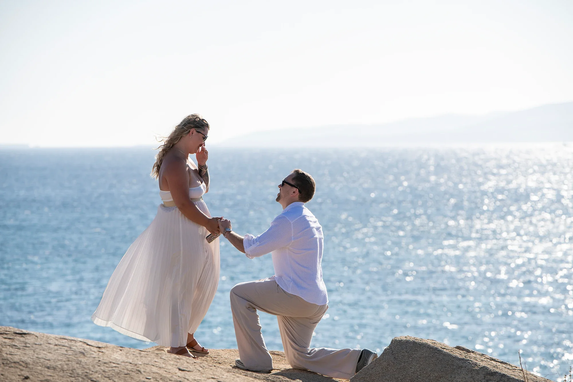 Man proposing on one knee by the sparkling Aegean Sea in Naxos
