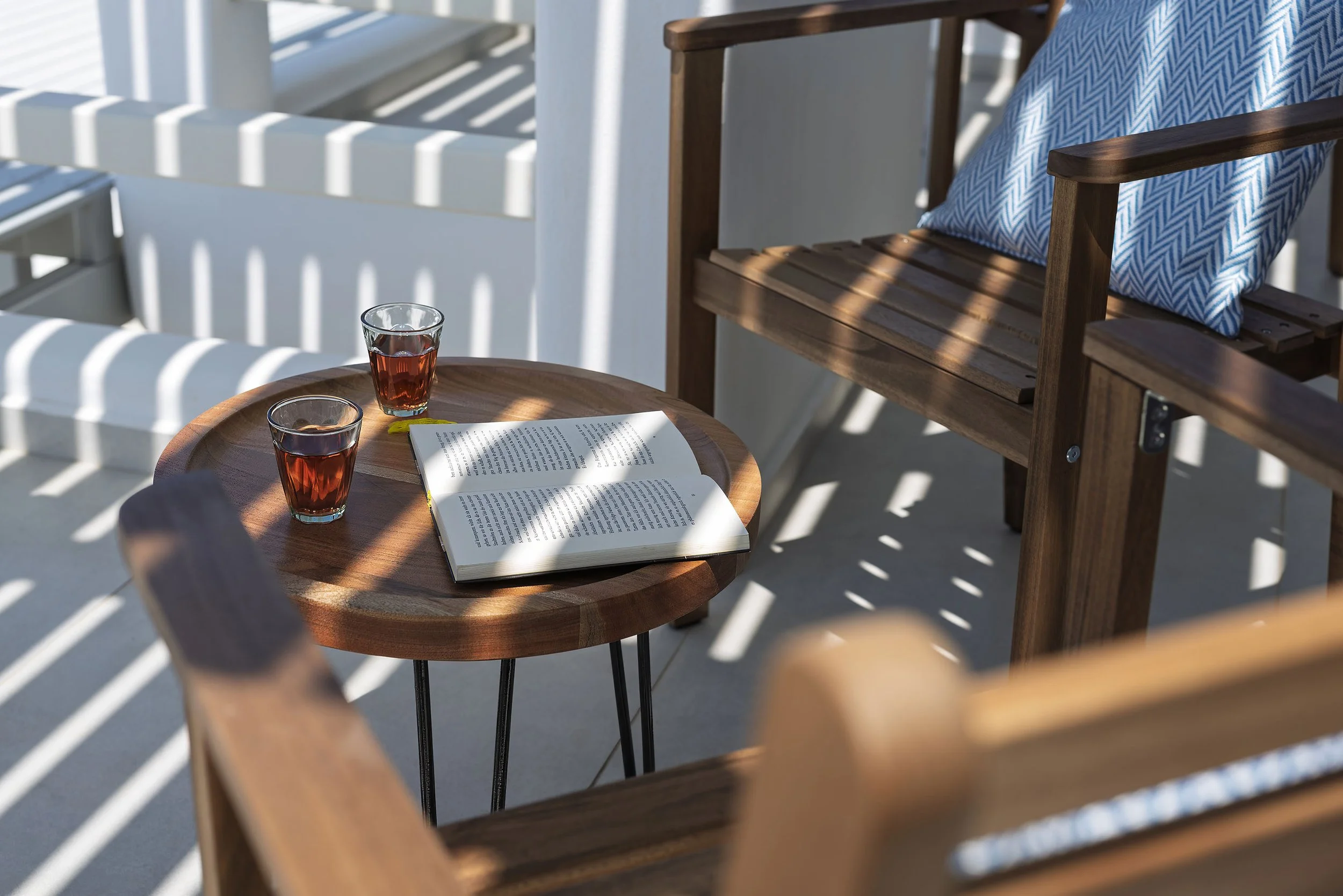 Inviting outdoor seating area with wooden chairs, a round coffee table, two glasses of tea, and a book, bathed in natural sunlight – perfect for showcasing the relaxed lifestyle of this Kastraki property in Naxos, Greece.