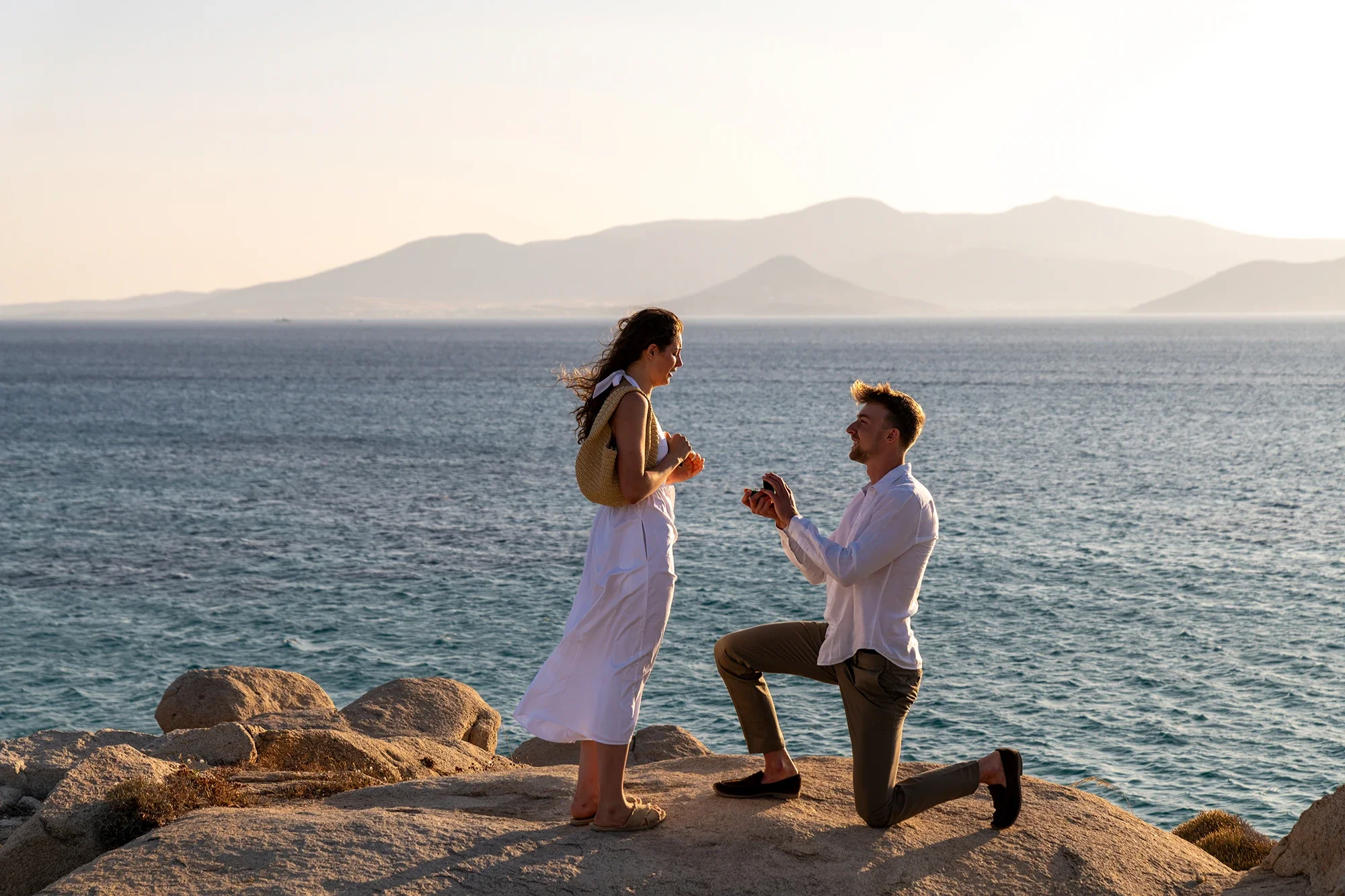 Man proposing on coastal rocks in Naxos during golden hour with mountain views