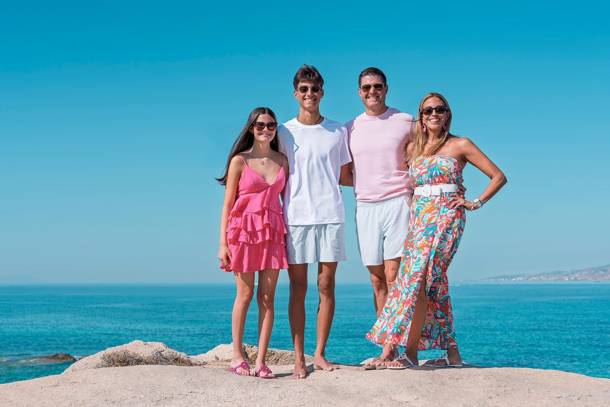Family of four standing on coastal rocks with the Aegean Sea in Naxos