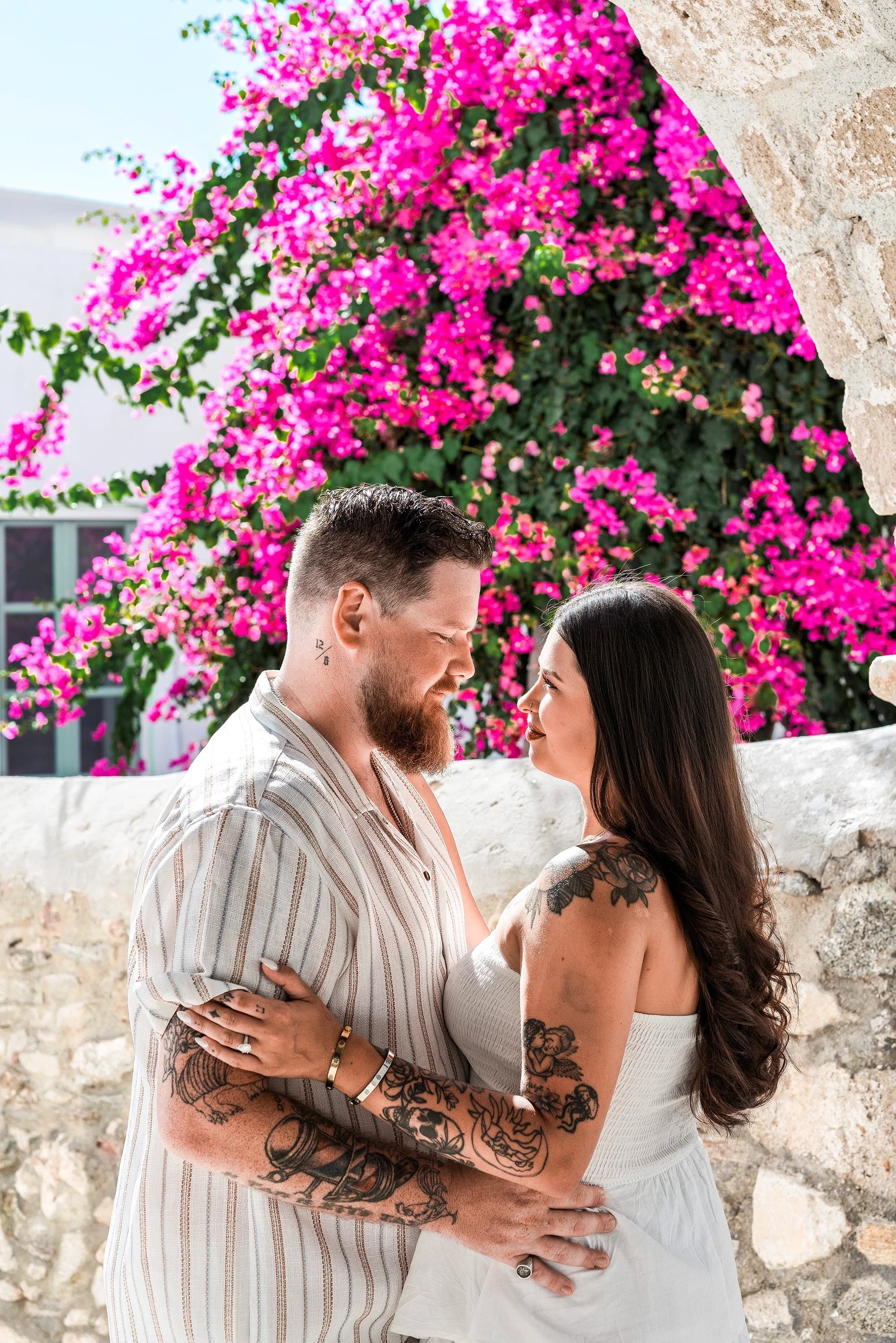 Couple embracing in front of a stone wall with bright pink bougainvillea in Naxos