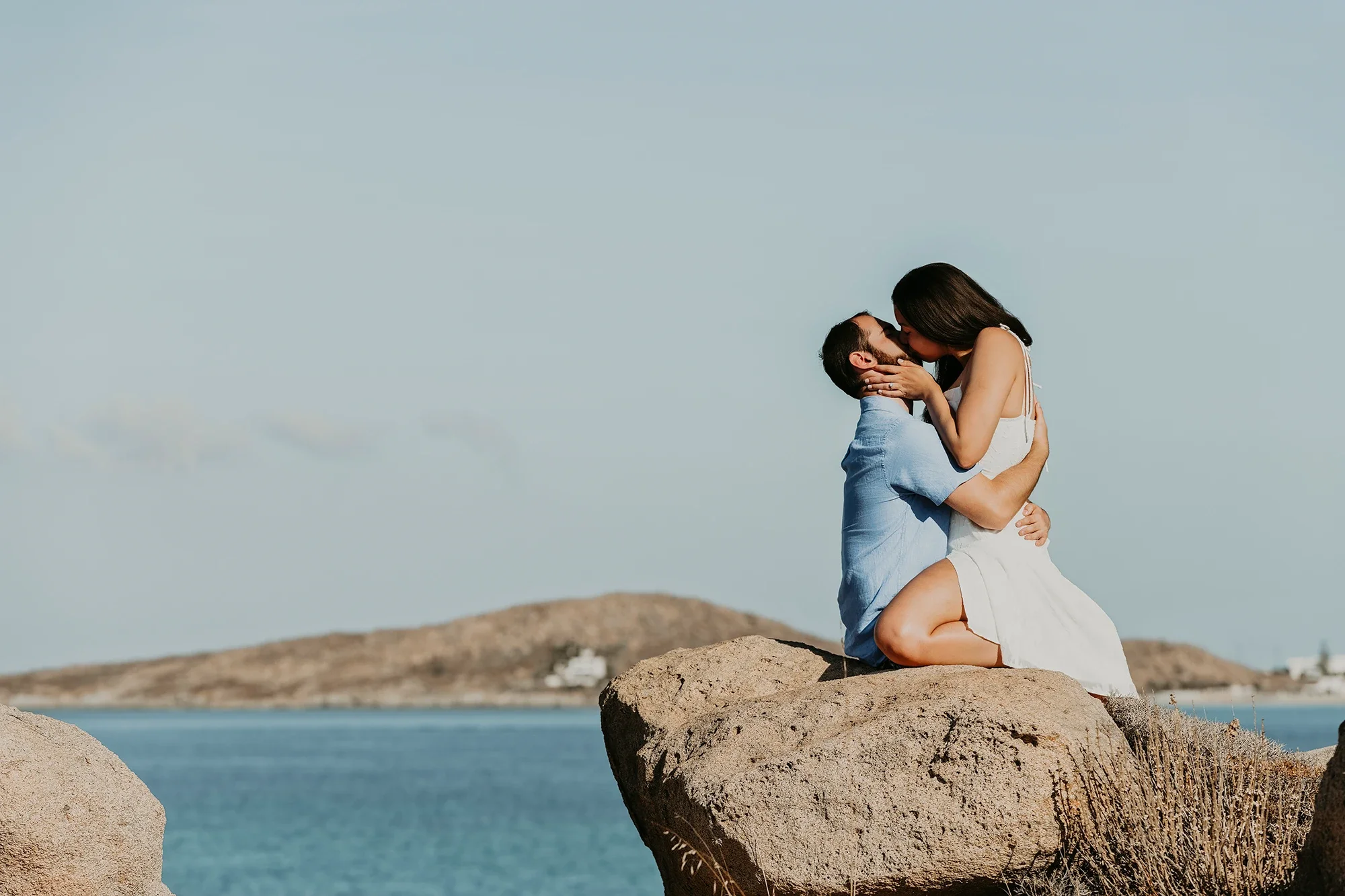 Couple kissing on coastal rocks in Naxos with island views in the background