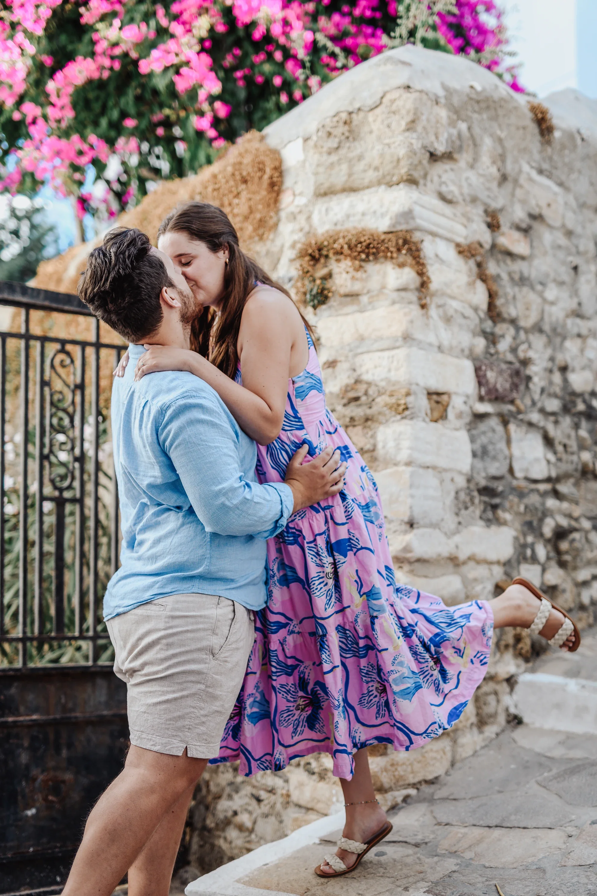 Couple kissing by a stone wall with pink bougainvillea in the Naxos Castle area