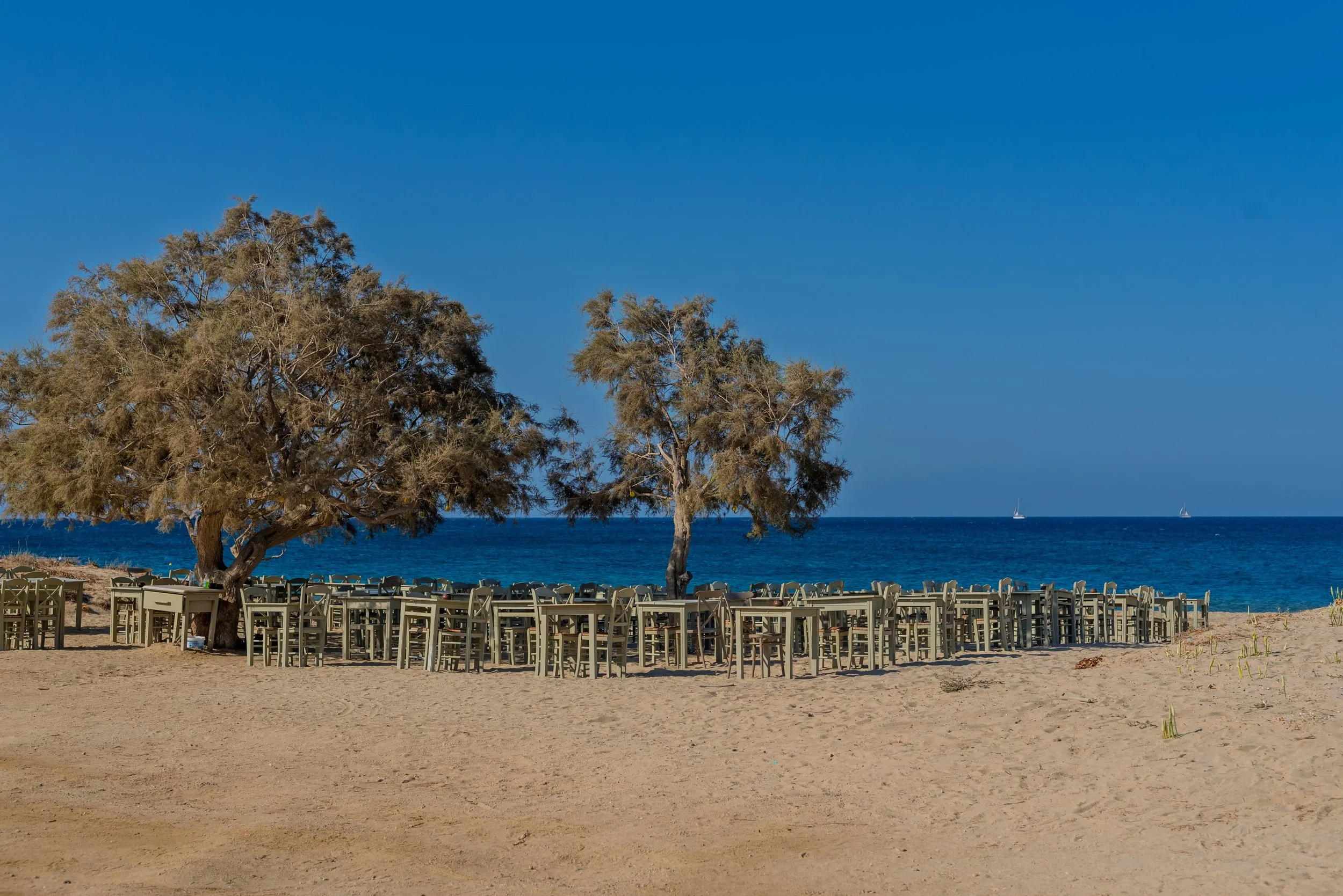 Landscape photography of Maragkas Beach in Naxos Greece with seaside taverna tables, sandy shore and deep blue Aegean Sea