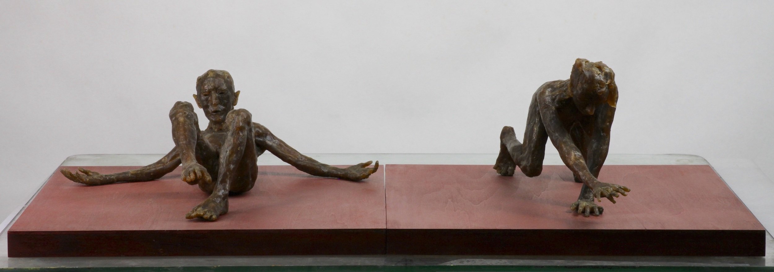 Two Figures on a Red Base (2022), microcrystalline wax, stained wood base, 6 x 24 x 12 inches