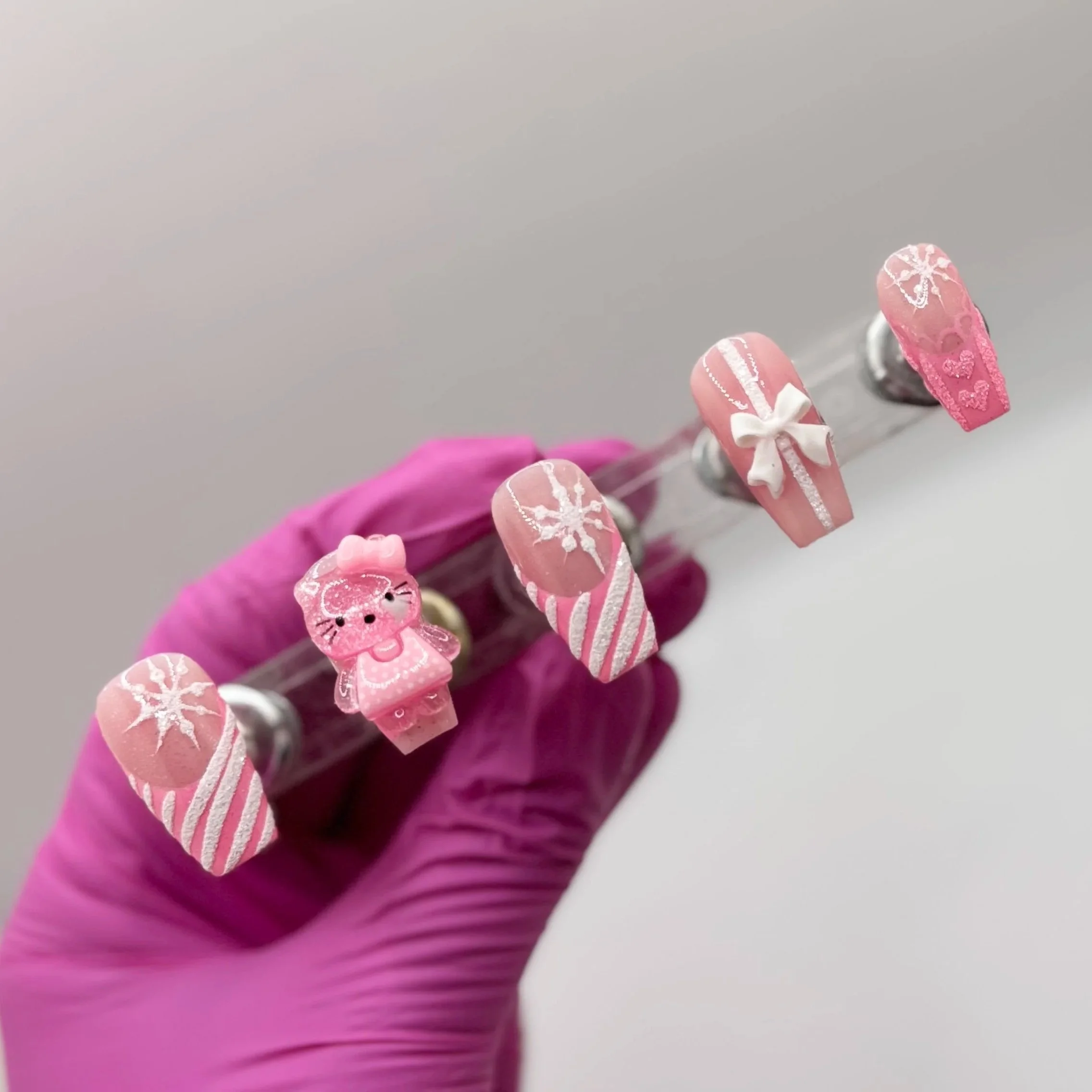 Pink Hello Kitty Christmas press-on nails with 3D Hello Kitty charm, white French tips, snowflakes, and holiday glitter detailing