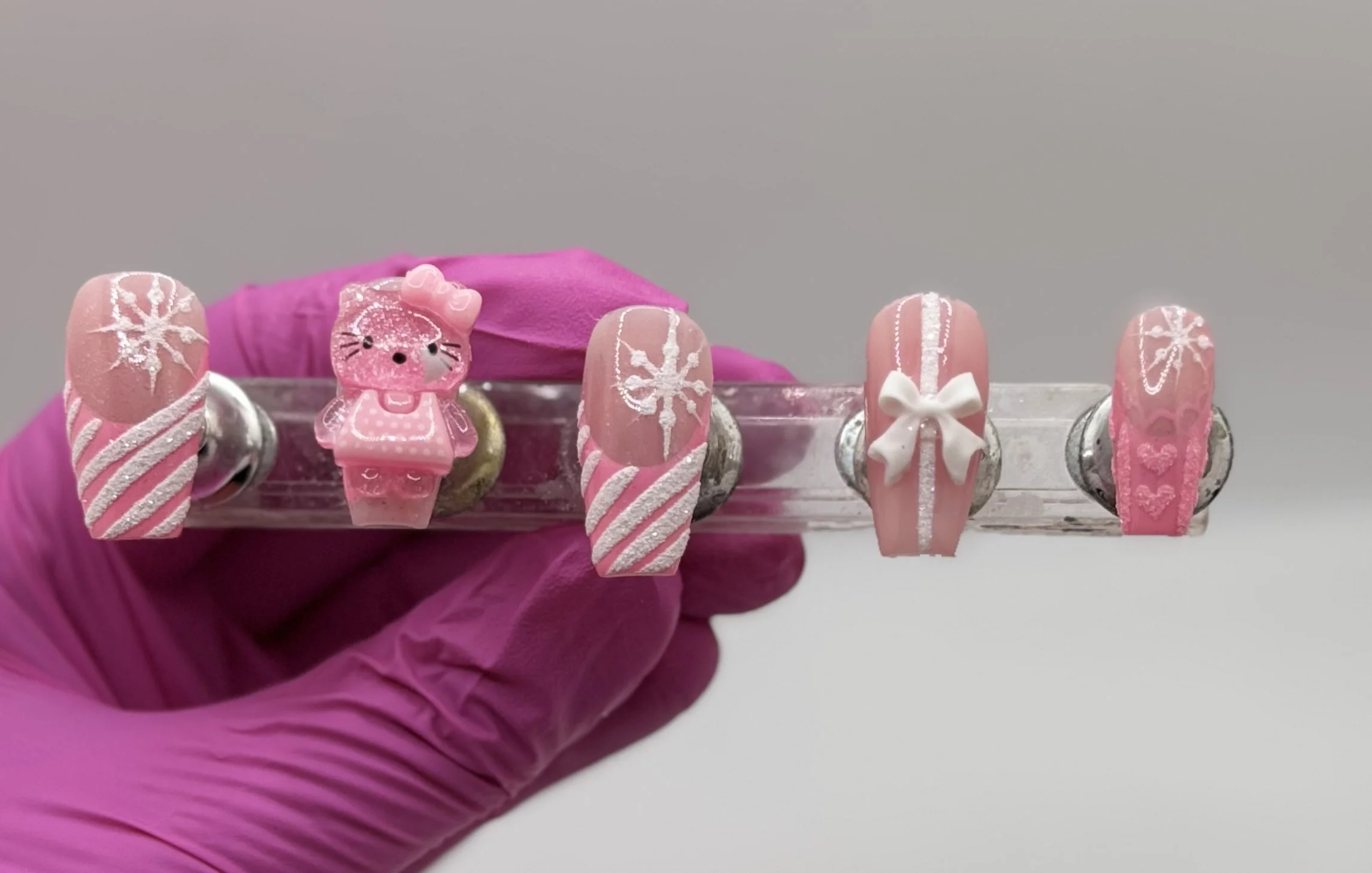 Close-up of 3D Hello Kitty Christmas nails featuring pink base, festive French tips, and sparkling holiday snowflake accents.