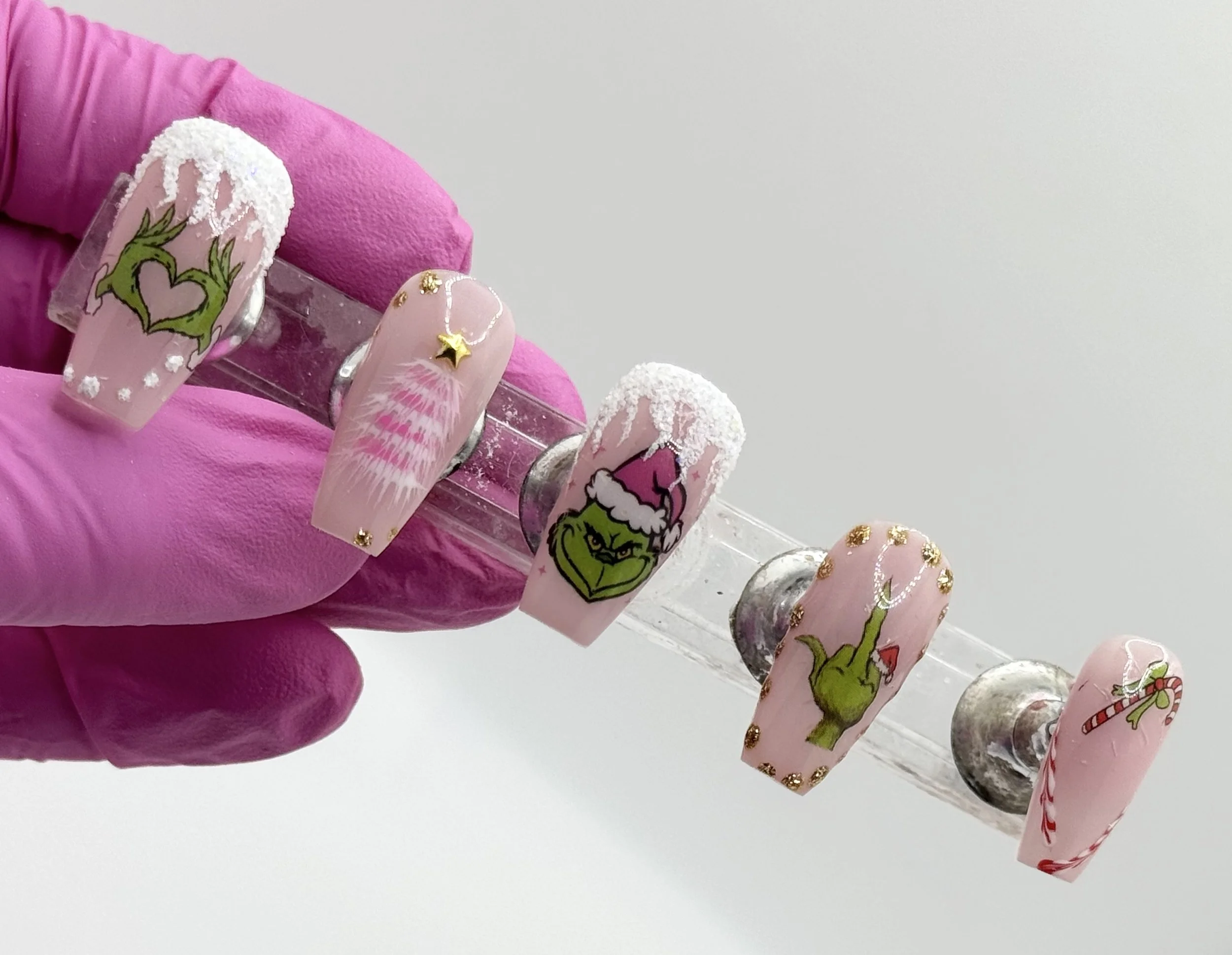 Pink Christmas nail set with glow snow, gold, Grinch elements, and playful pink tree decorations