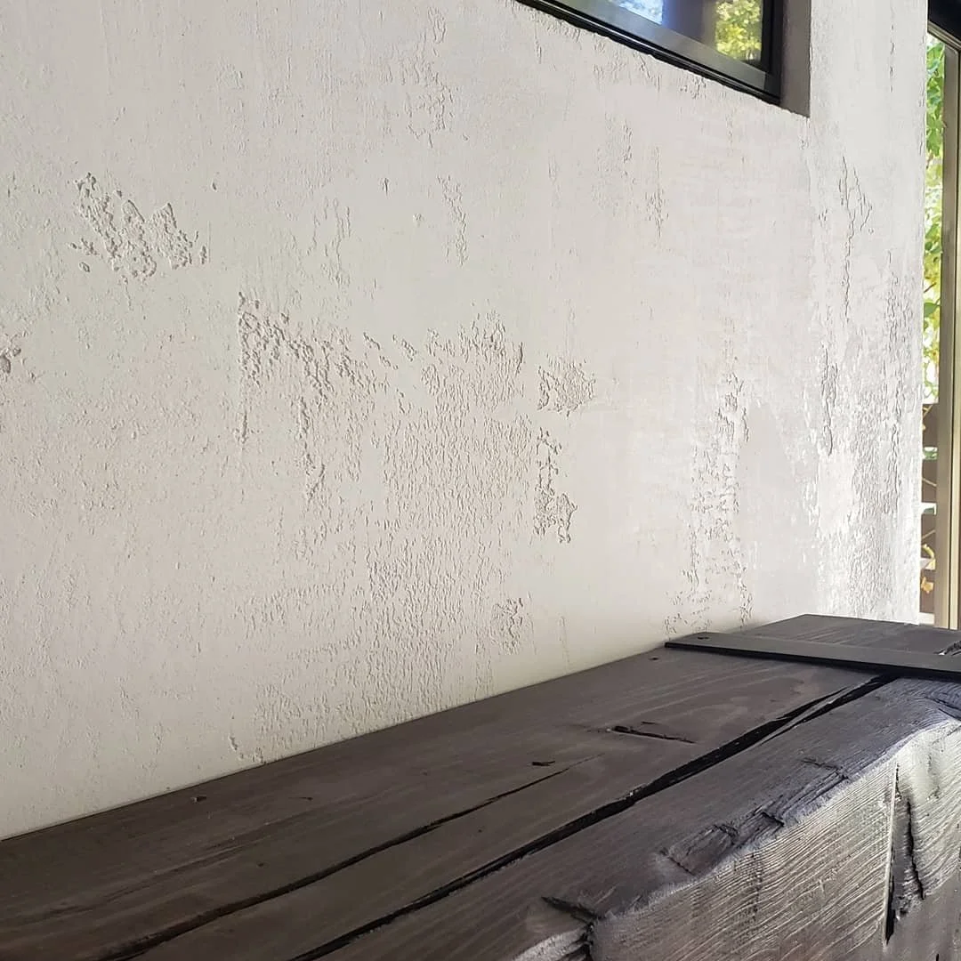 A textured white wall with a small window at the top right and a weathered wooden surface at the bottom.