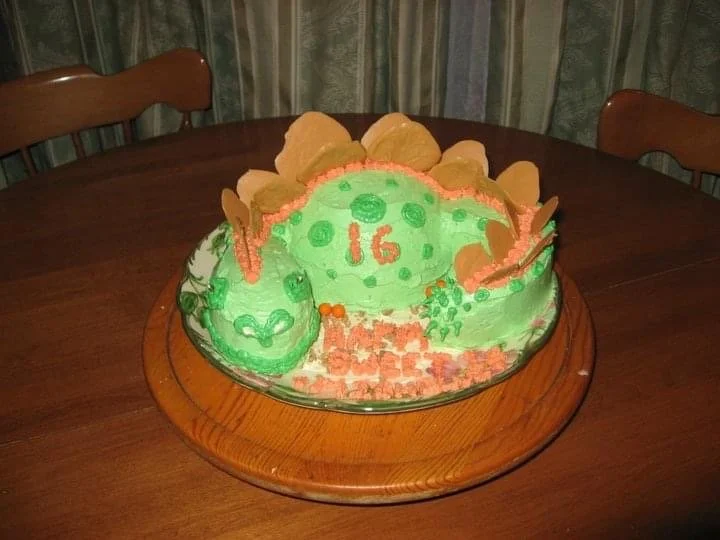 Colorful children's birthday cake with green icing, orange decorations, and a number 16, placed on a wooden table.