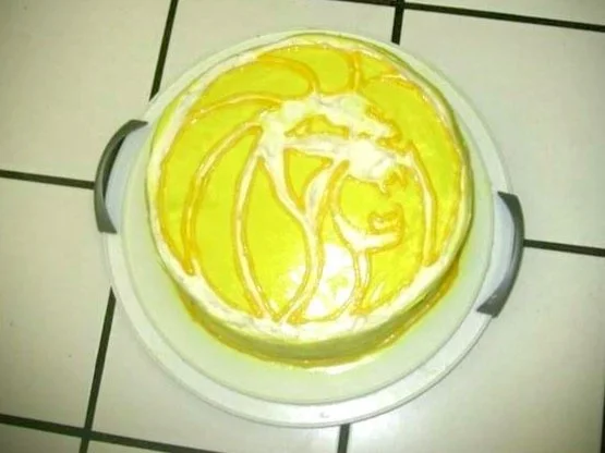 A round cake with yellow and white icing, decorated with a swirling pattern, on a white tile surface.