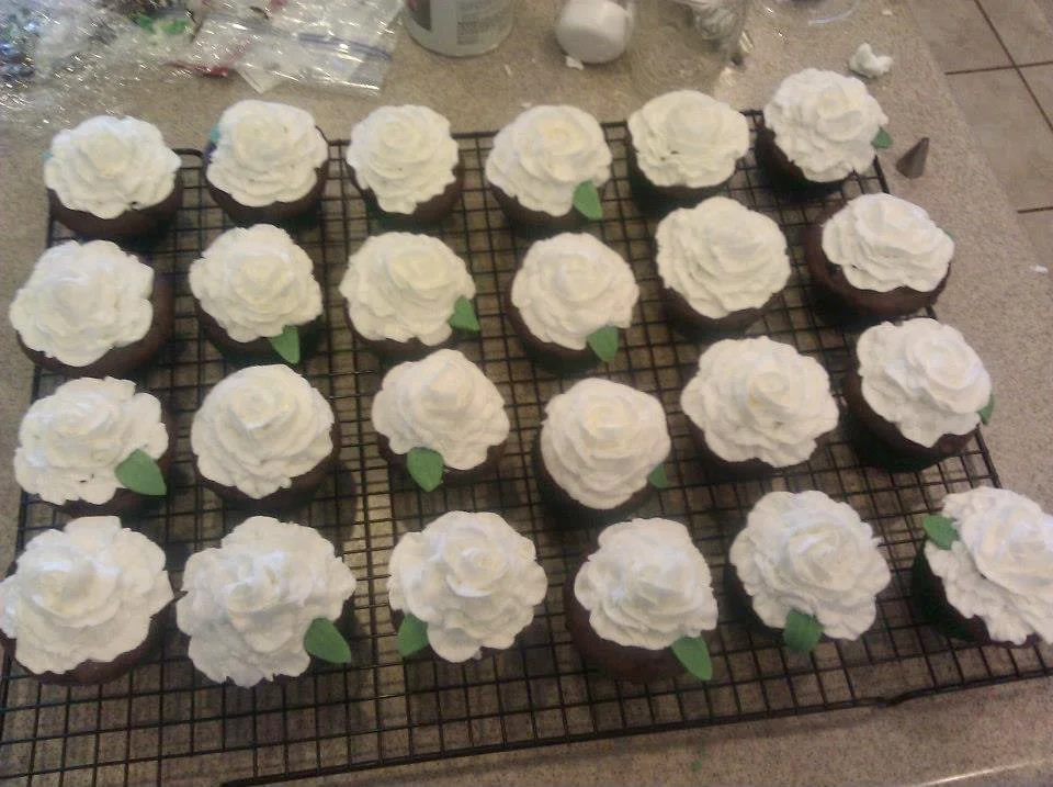 Chocolate cupcakes with white frosting and small green leaf decorations on top, arranged on a cooling rack.